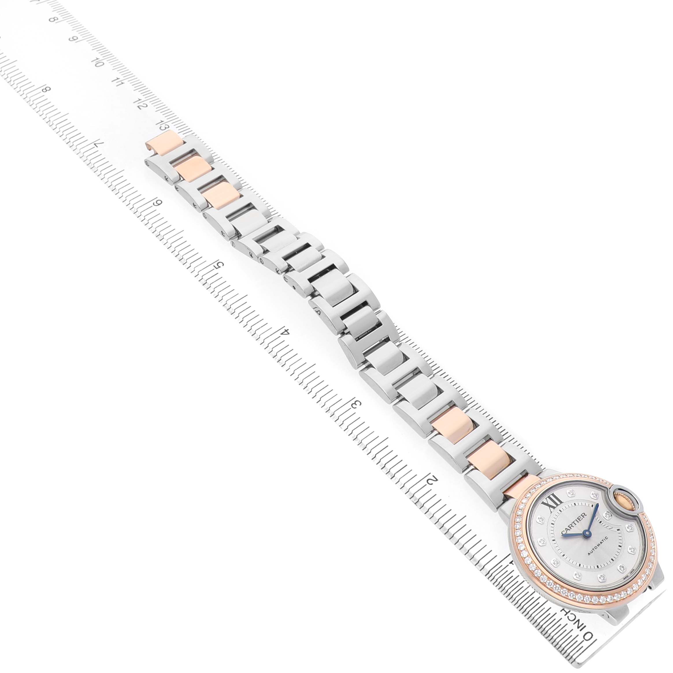 The Cartier Ballon Bleu WE902077 Women's Steel and Gold (two tone) Silver Dial watch is shown from an angled top view, displaying the face and bracelet alongside a ruler.