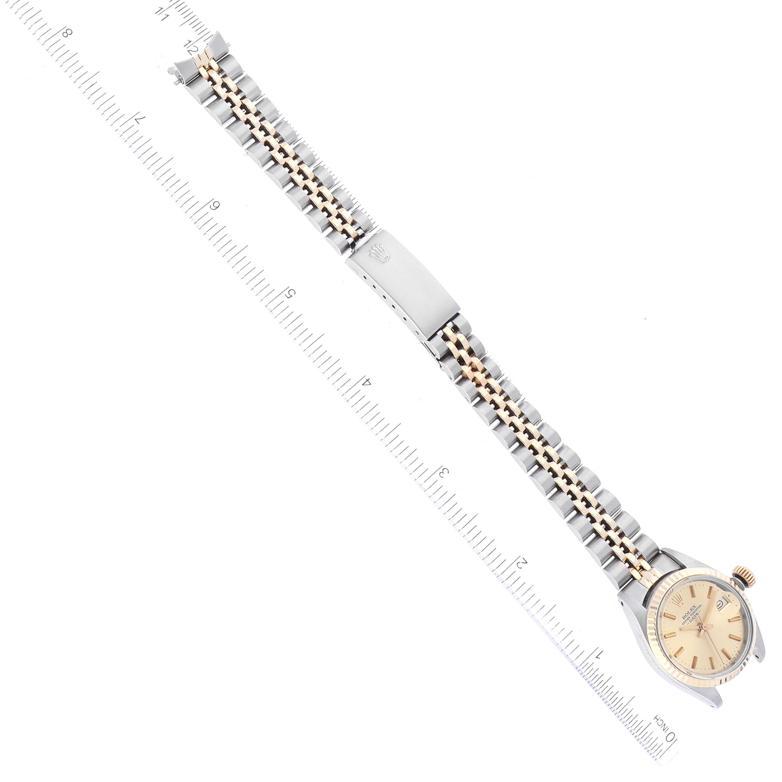 The image shows a top-down view of a Rolex Date 6917 Women's Steel and Gold (two tone) Champagne Dial 6917 Women's Steel and Gold (two tone) Champagne Dial model watch, displaying the face, bezel, and bracelet with a ruler for scale.