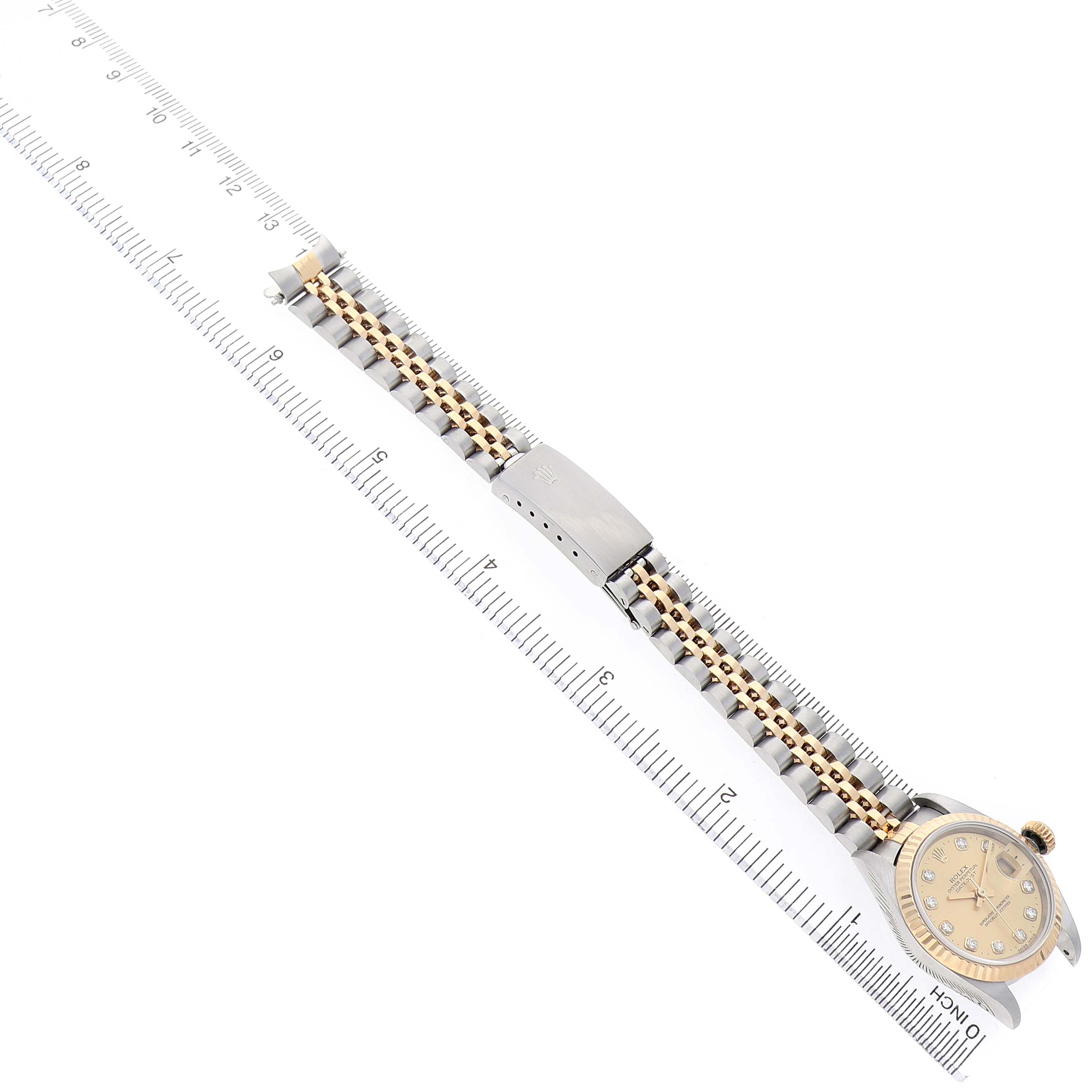 The Rolex Datejust 69173 Women's Steel and Gold (two tone) Champagne Dial watch is shown at a diagonal angle, featuring its dial, bracelet, and clasp alongside a ruler for scale.