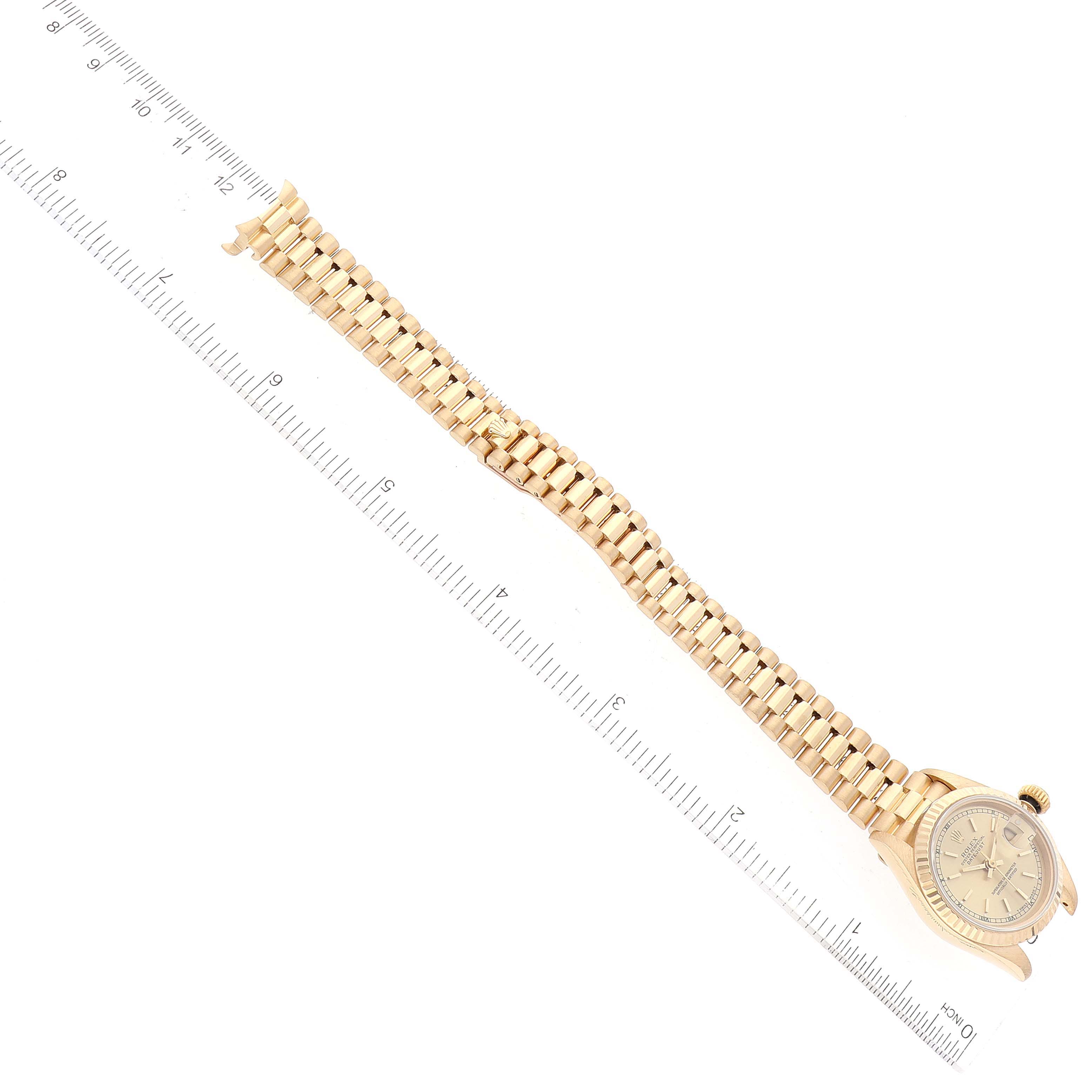 The image shows a Rolex President 69178 Women
s Yellow Gold Champagne Dial 69178 Women
s Yellow Gold Champagne Dial model wristwatch laid flat next to a ruler, showcasing the watch face and the entire bracelet length.