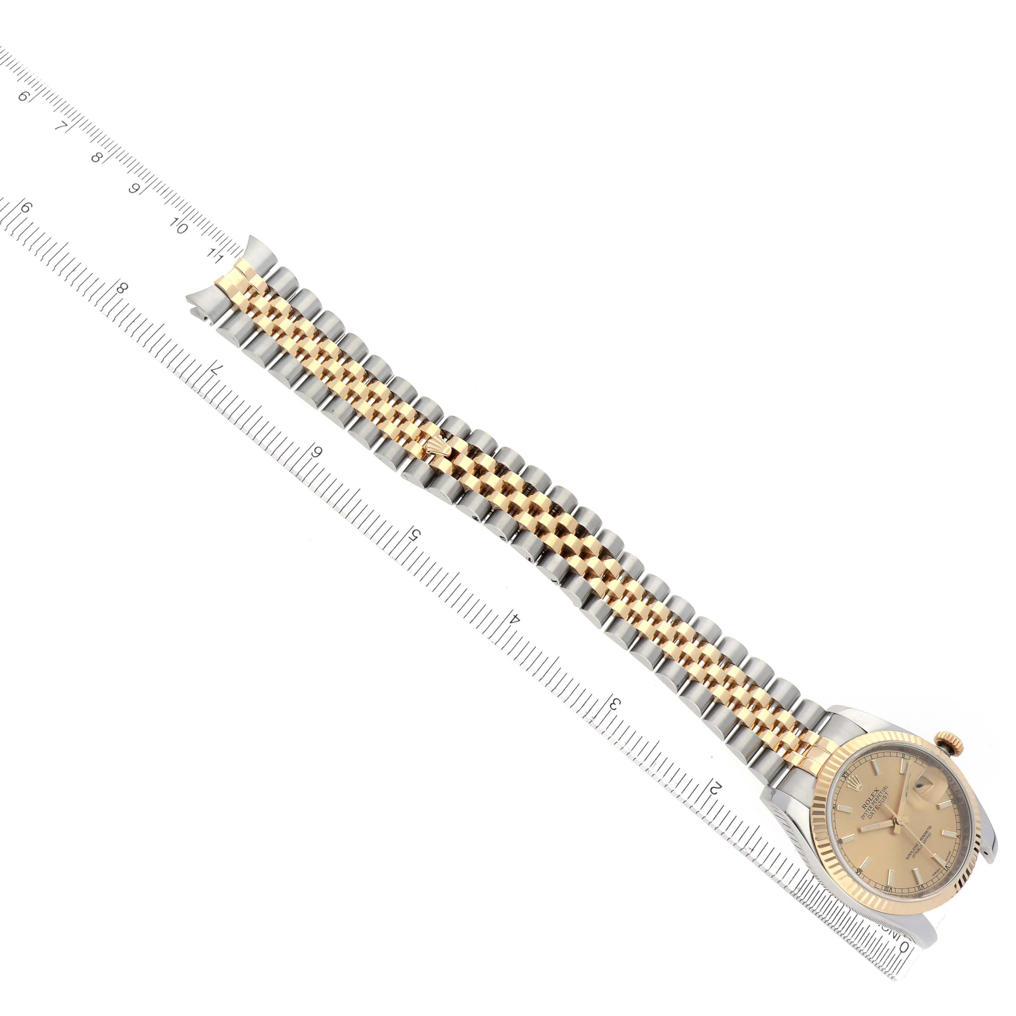 The Rolex Datejust 116233 Men
s Steel and Gold (two tone) Champagne Dial 116233 Men
s Steel and Gold (two tone) Champagne Dial watch is shown from an overhead angle, highlighting the watch face, two-tone bracelet, and a ruler for scale.