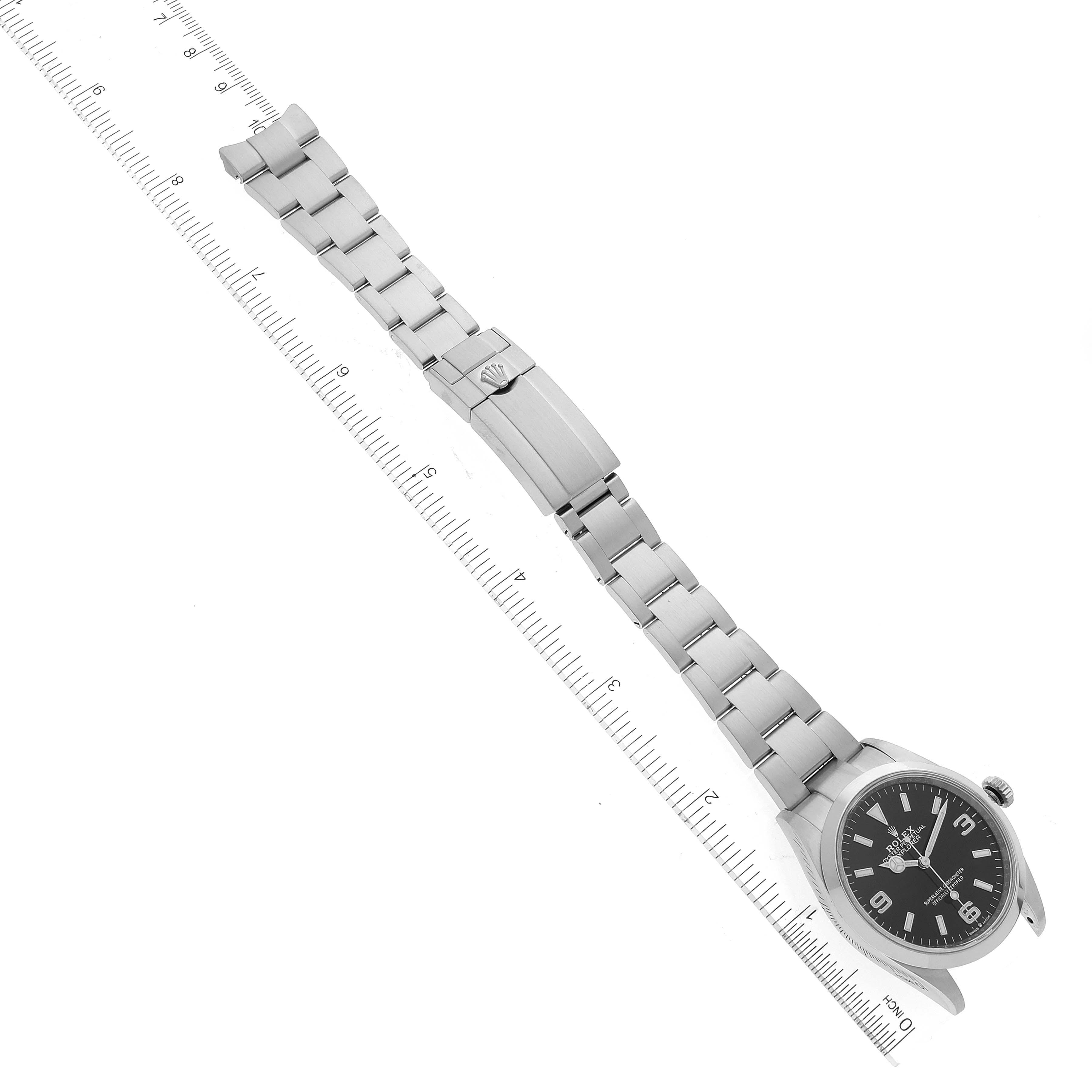 The image shows a top-down view of a Rolex Explorer 124270 Men's Stainless Steel Black Dial 124270 Men's Stainless Steel Black Dial watch, including its dial, bracelet, and clasp next to a measurement ruler.