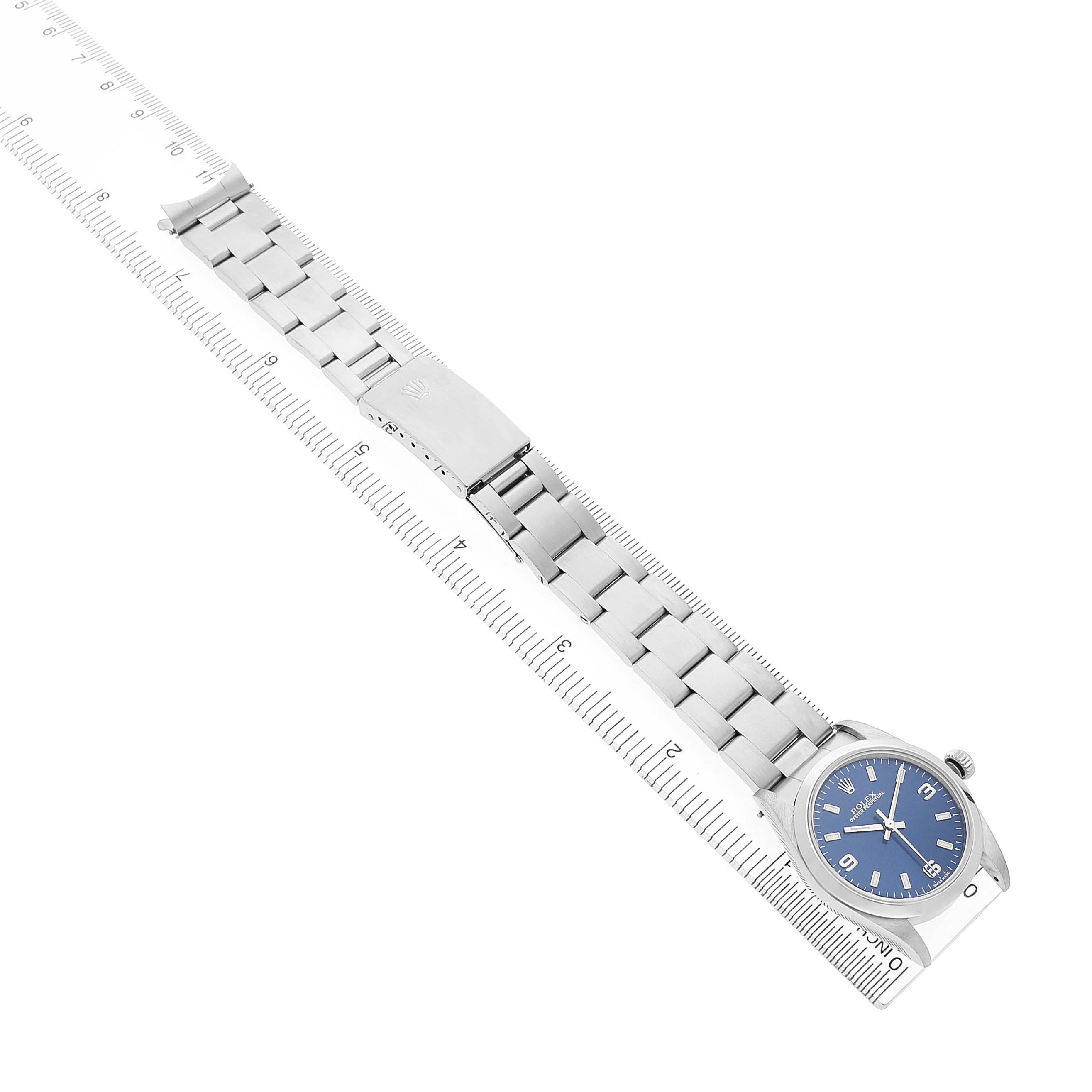 The image shows the Rolex Mid-Size 77080 Women's Stainless Steel Blue Dial watch from an elevated side angle, displaying its face and full bracelet laid alongside a ruler.