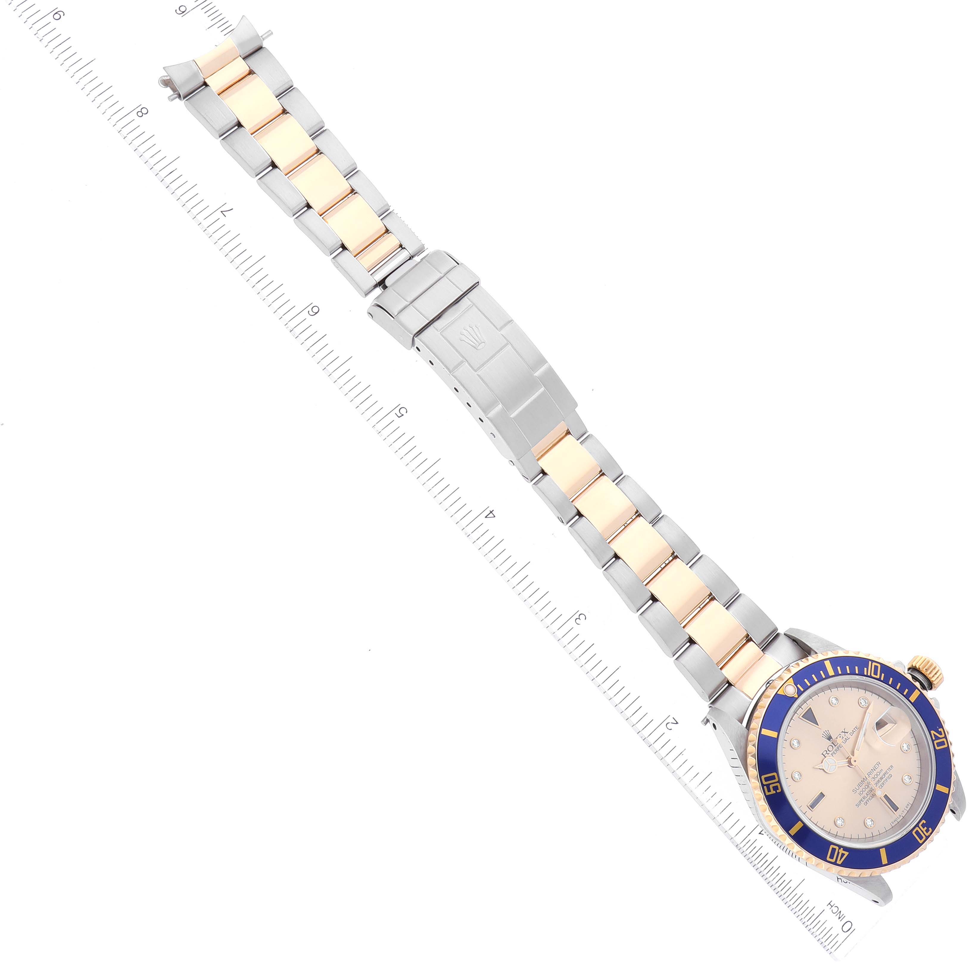 This image shows a Rolex Submariner 16613 Men's Steel and Gold (two tone) Champagne Dial 16613 Men's Steel and Gold (two tone) Champagne Dial watch laid flat with a ruler along its length, highlighting the bezel, dial, and bracelet.