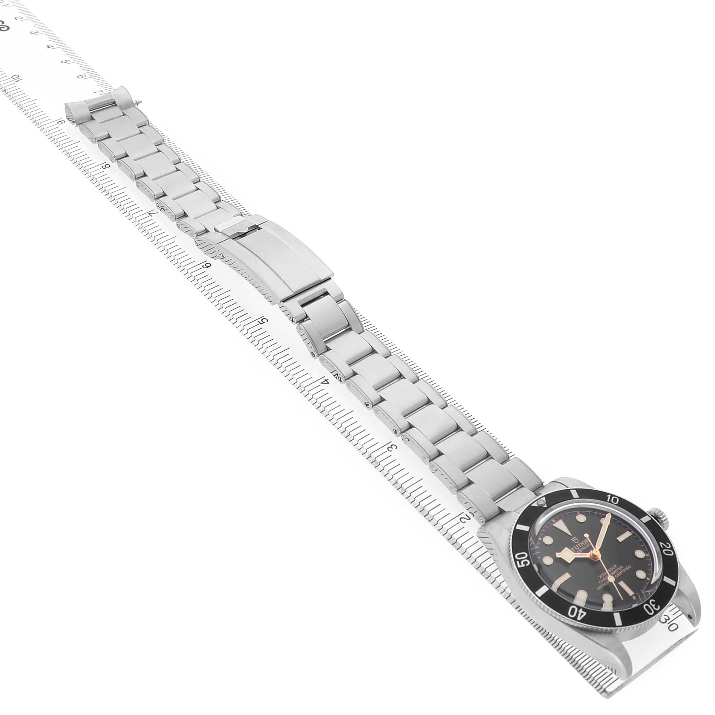 The Tudor Heritage Black Bay M79000N Men's Stainless Steel Black Dial watch is shown at a diagonal angle, displaying the face, bezel, bracelet, and deployment clasp.