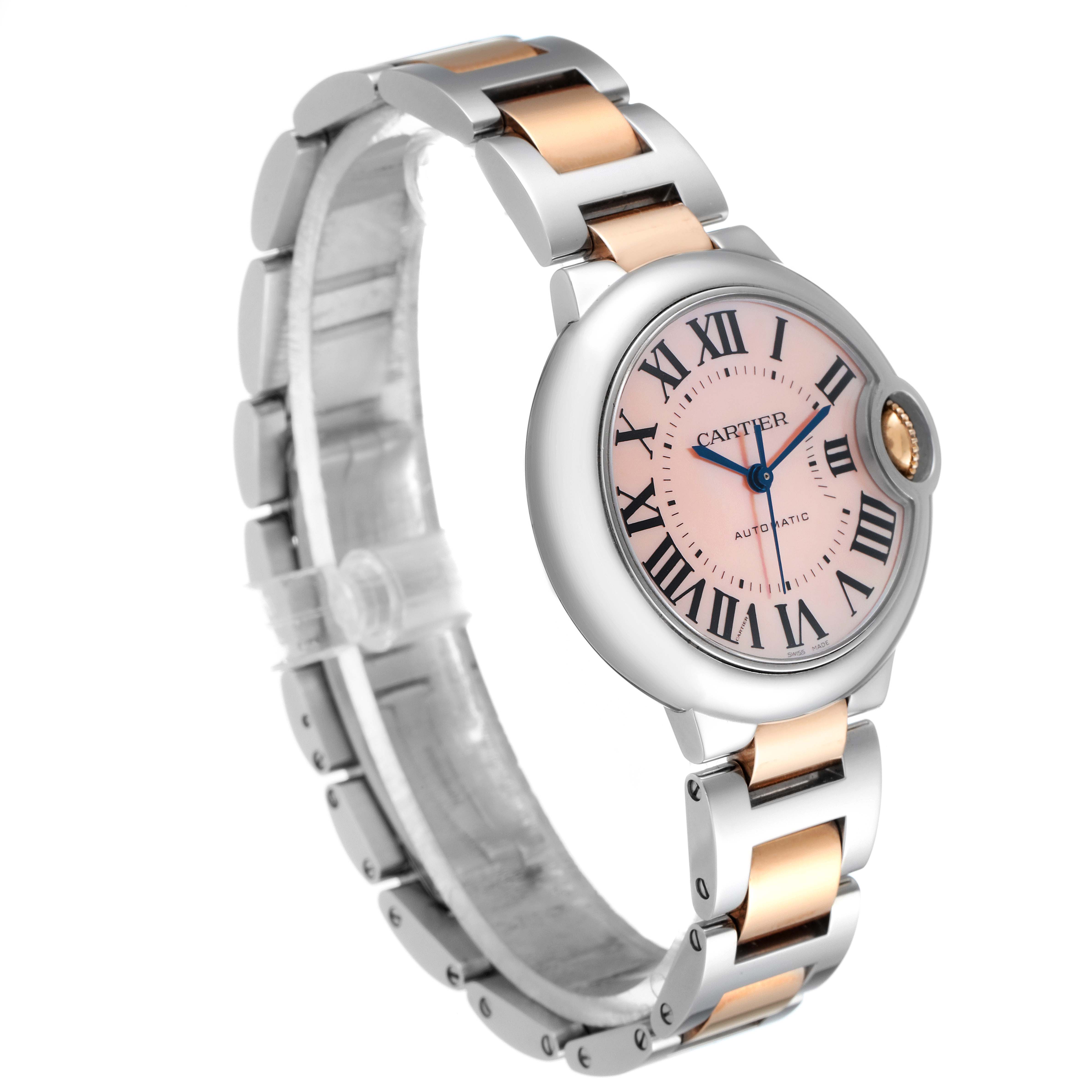 The image shows a side angle of the Cartier Ballon Bleu W6920098 Women's Steel and Gold (two tone) Mother of Pearl Dial W6920098 Women's Steel and Gold (two tone) Mother of Pearl Dial watch, featuring its round case, pink dial, and two-tone metal bracelet.