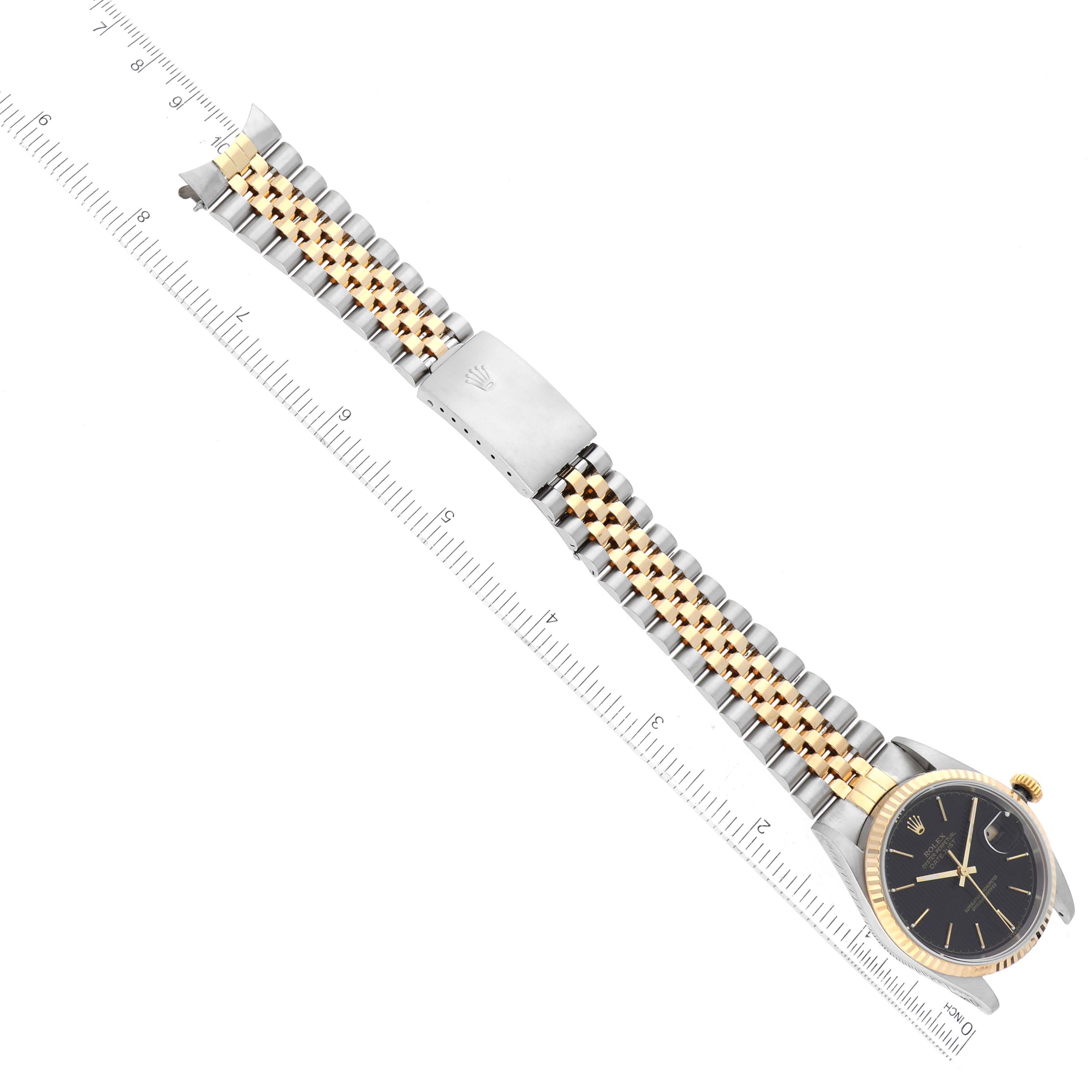 The image shows a top view of a Rolex Datejust 16233 Men's Steel and Gold (two tone) Black Dial 16233 Men's Steel and Gold (two tone) Black Dial watch with a black dial and two-tone Jubilee bracelet placed beside a ruler.