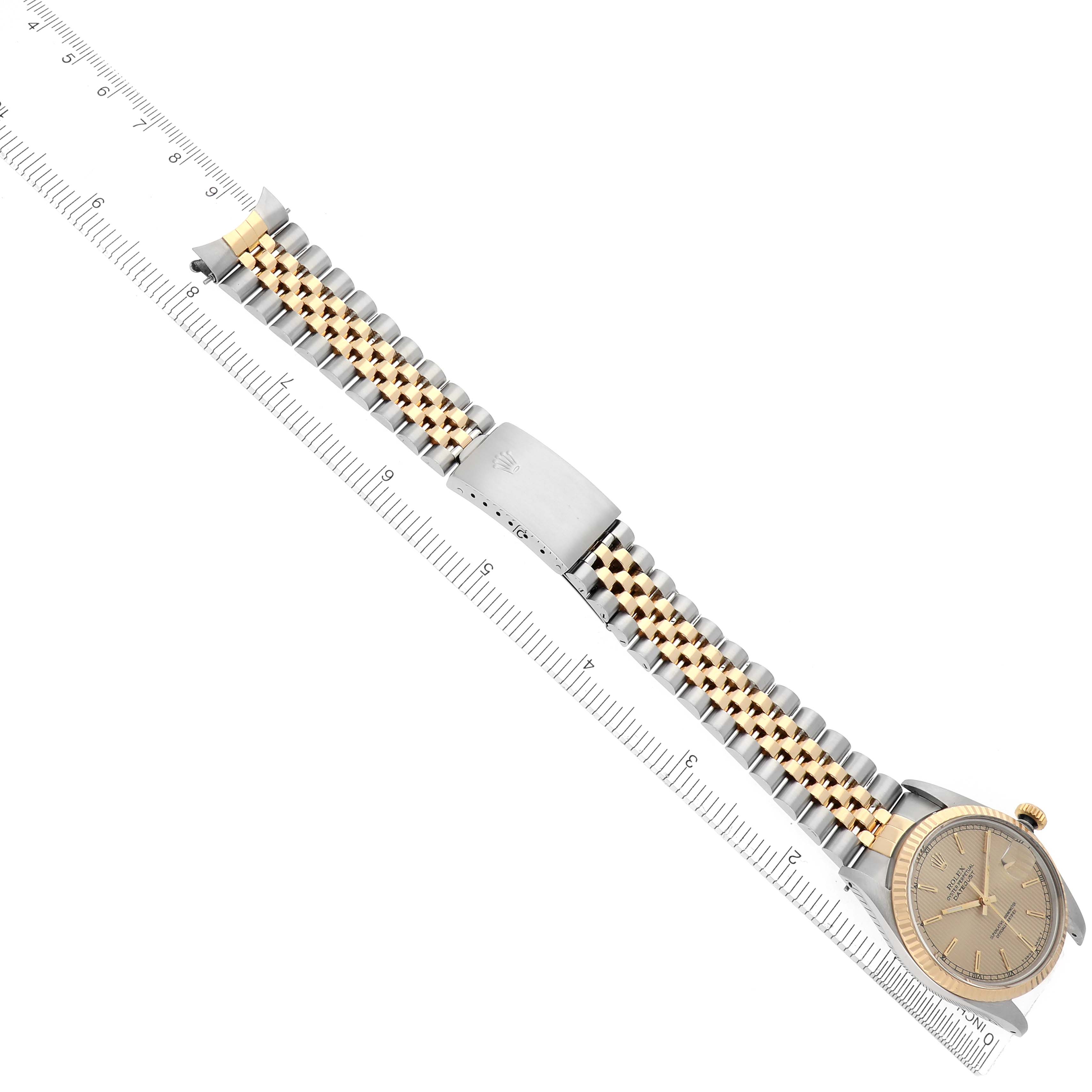 The Rolex Datejust 16013 Men
s Steel and Gold (two tone) Champagne Dial 16013 Men
s Steel and Gold (two tone) Champagne Dial watch is shown diagonally, displaying its face, bracelet, and clasp alongside a ruler for scale.