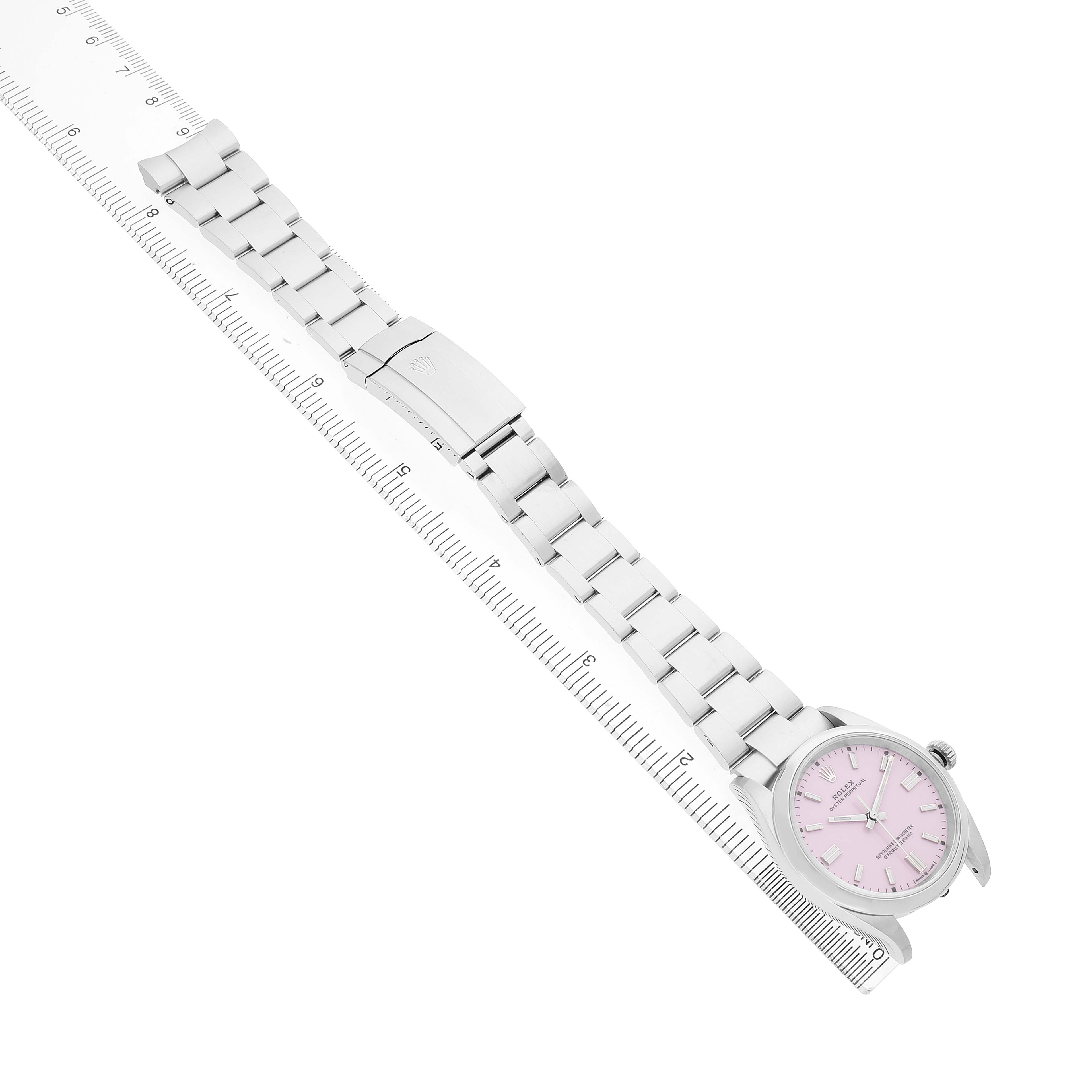 The Rolex Oyster Perpetual 126000 Men's Stainless Steel Pink Dial watch is shown from an angled top view, displaying the full bracelet and pink dial face placed alongside a ruler.