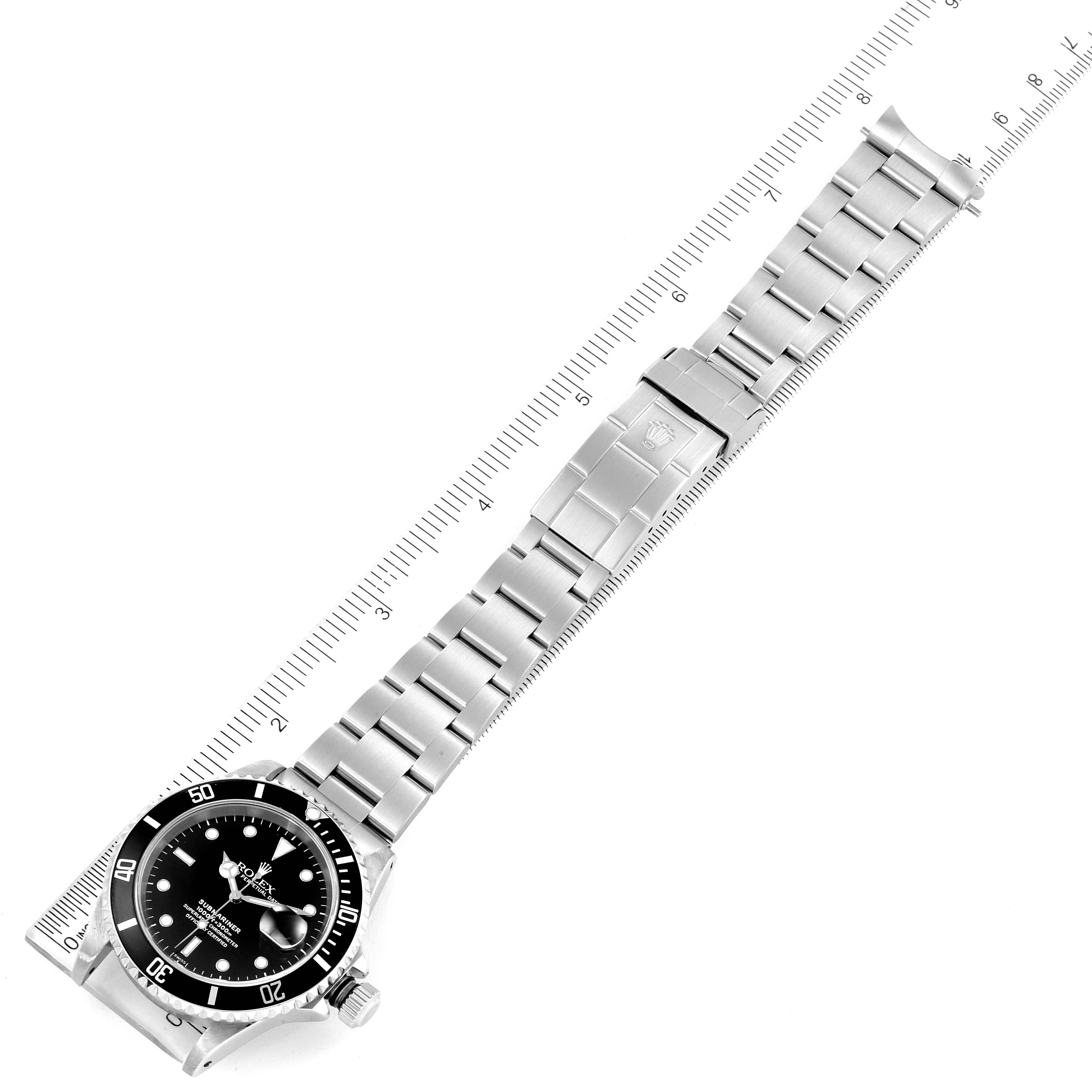 The image shows a top-down view of the Rolex Submariner 16610 Men
s Stainless Steel Black Dial 16610 Men
s Stainless Steel Black Dial watch, displaying its bracelet, clasp, and dial alongside a ruler for scale.