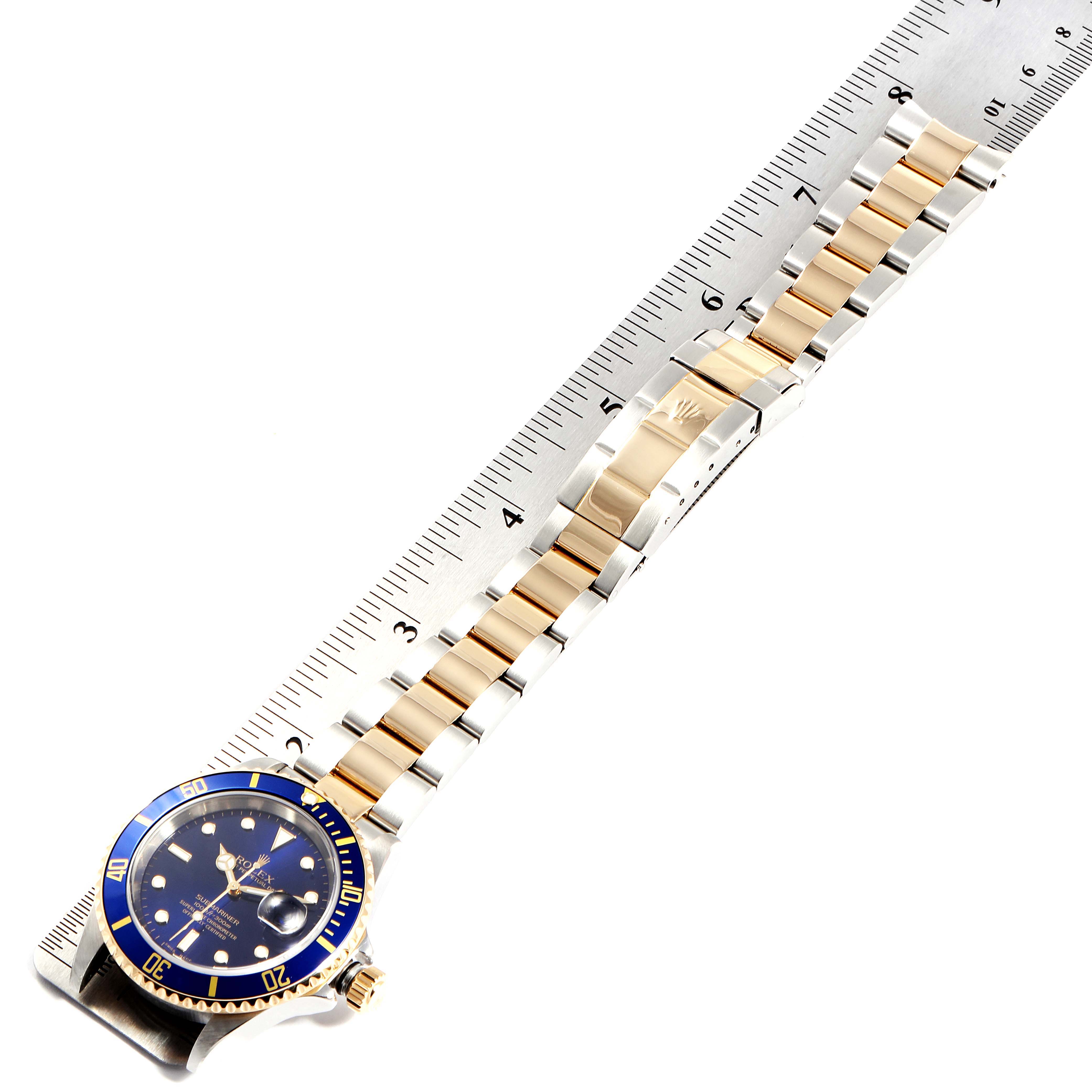 The image shows a Rolex Submariner 16613 Men
s Steel and Gold (two tone) Blue Dial 16613 Men
s Steel and Gold (two tone) Blue Dial watch laid flat, showcasing the dial, bezel, and bracelet, measured against a ruler.