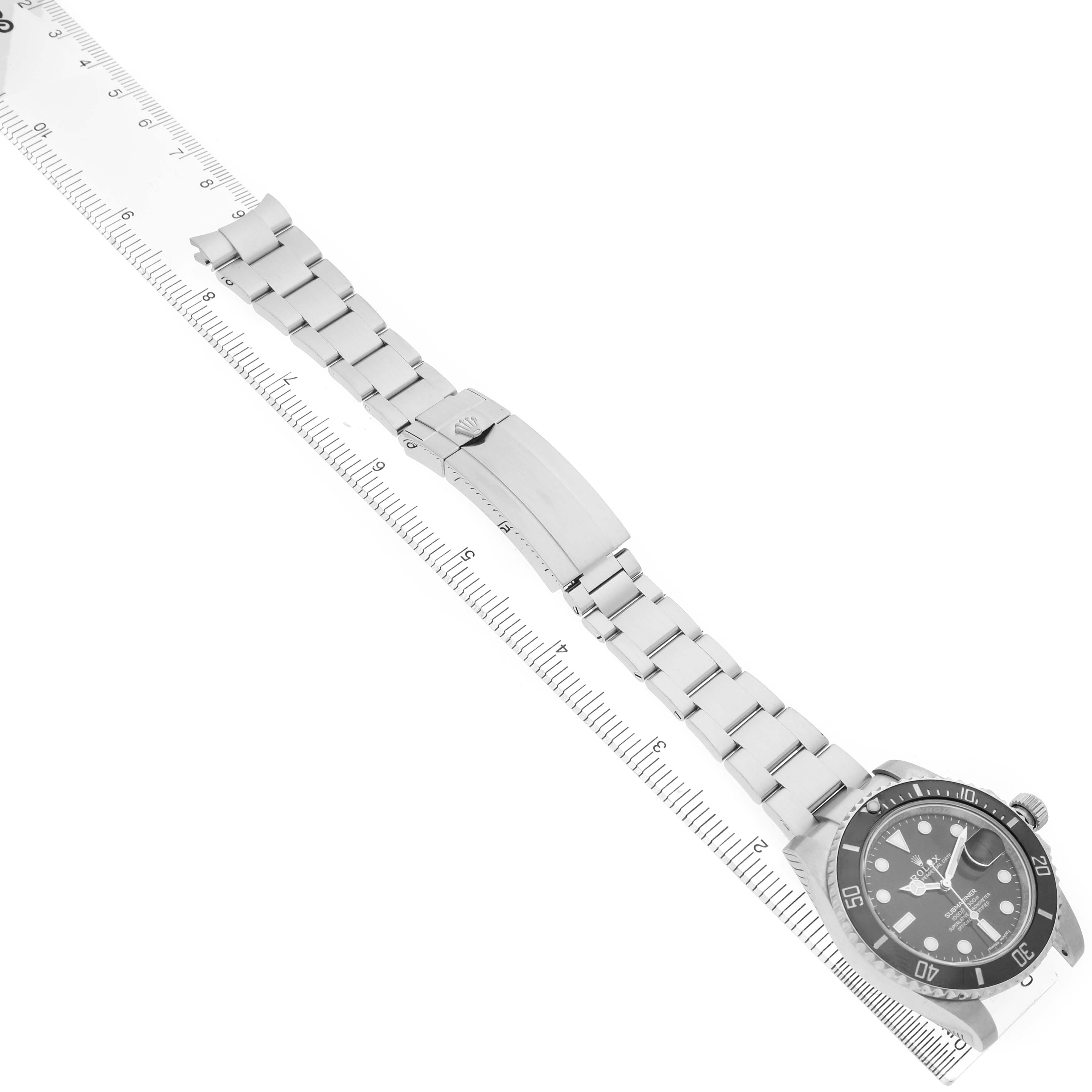 The image shows a Rolex Submariner 116610 Men's Stainless Steel Black Dial watch laid flat with its bracelet extended, positioned alongside a ruler at a diagonal angle.