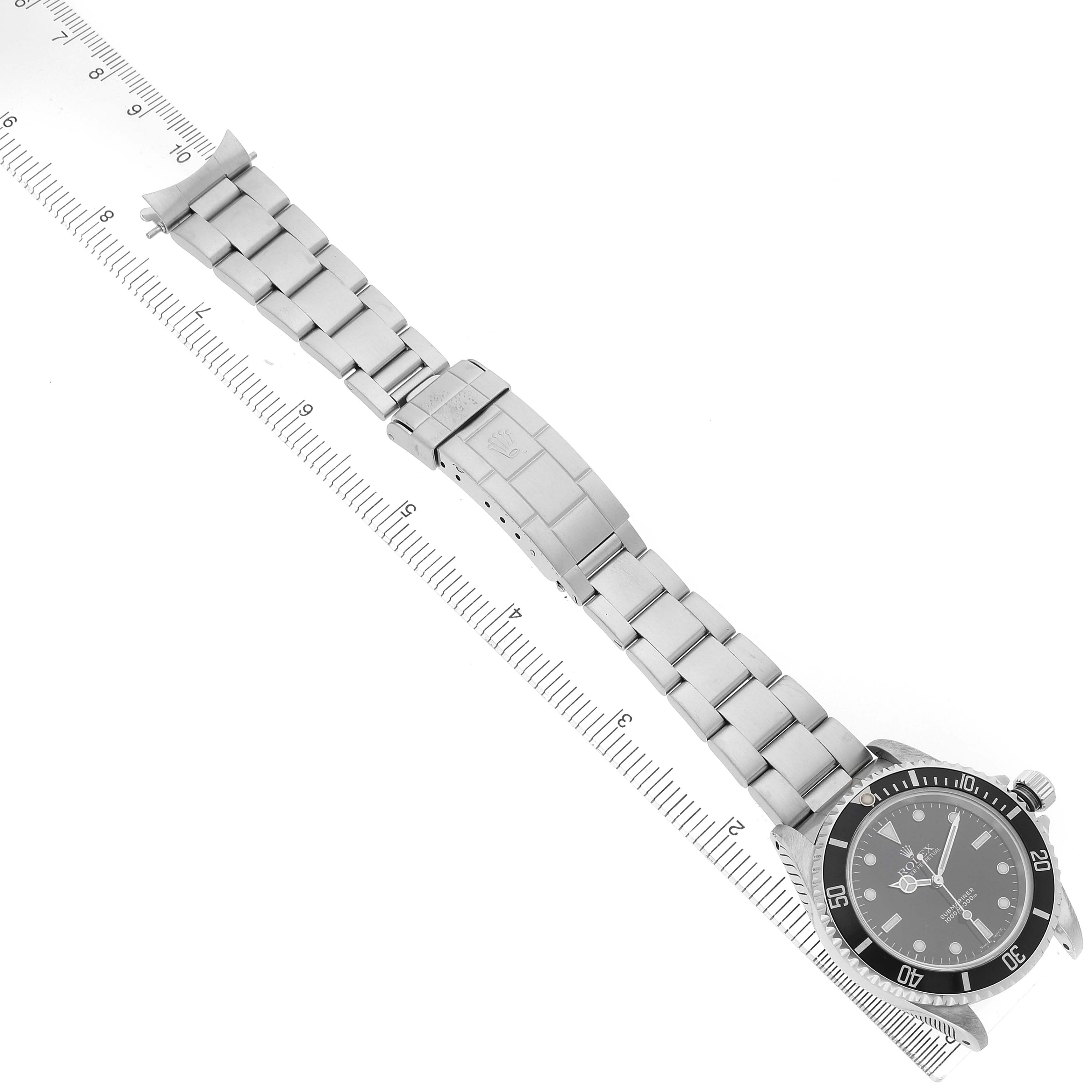 The Rolex Submariner 14060 Men's Stainless Steel Black Dial watch is photographed from above, showing the full bracelet, clasp, and face next to a ruler.