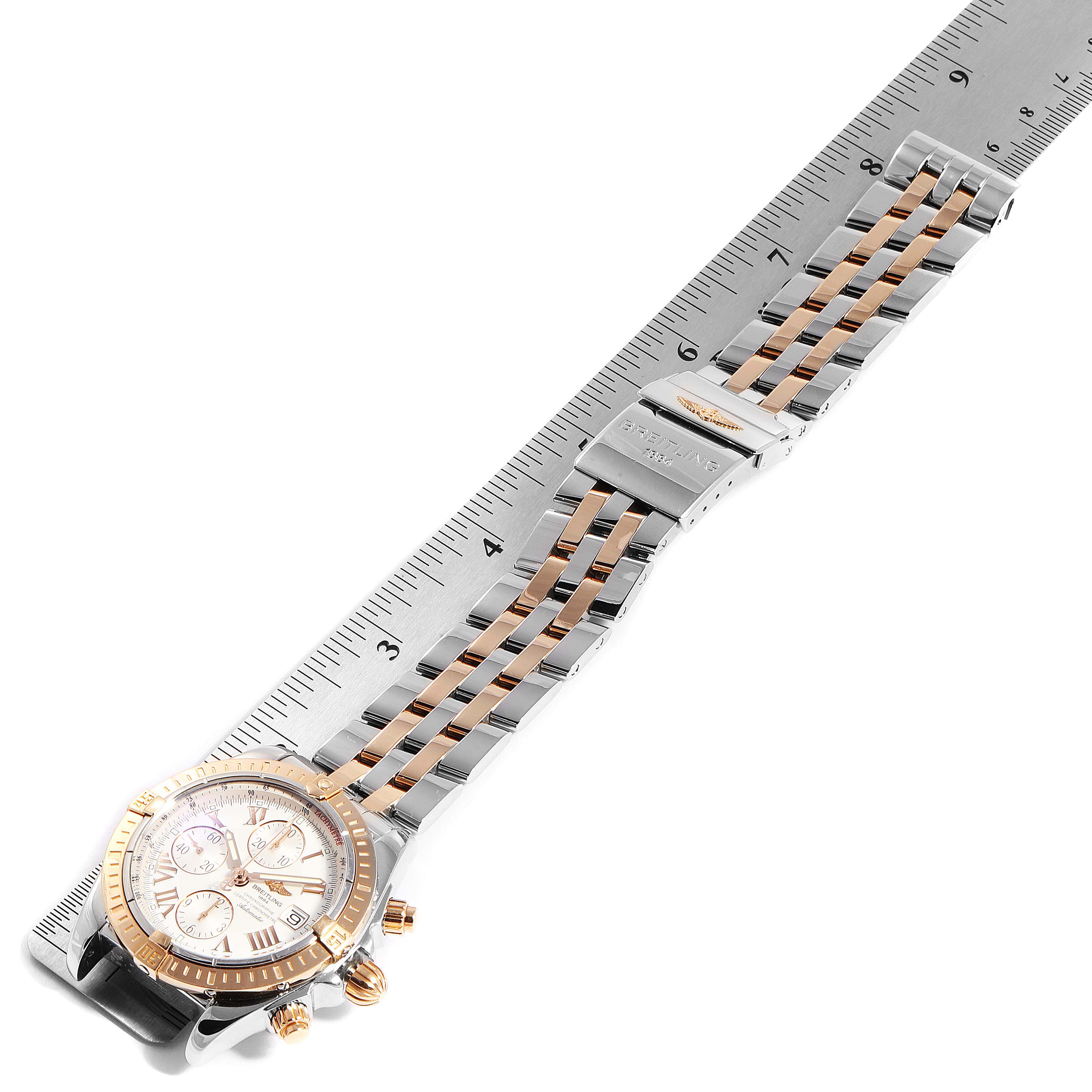 The image shows a Breitling Chronomat C13356 Men's Steel and Gold (two tone) White Dial C13356 Men's Steel and Gold (two tone) White Dial watch from an angled top-down view, displaying the face, bezel, bracelet, and clasp lying on a ruler.