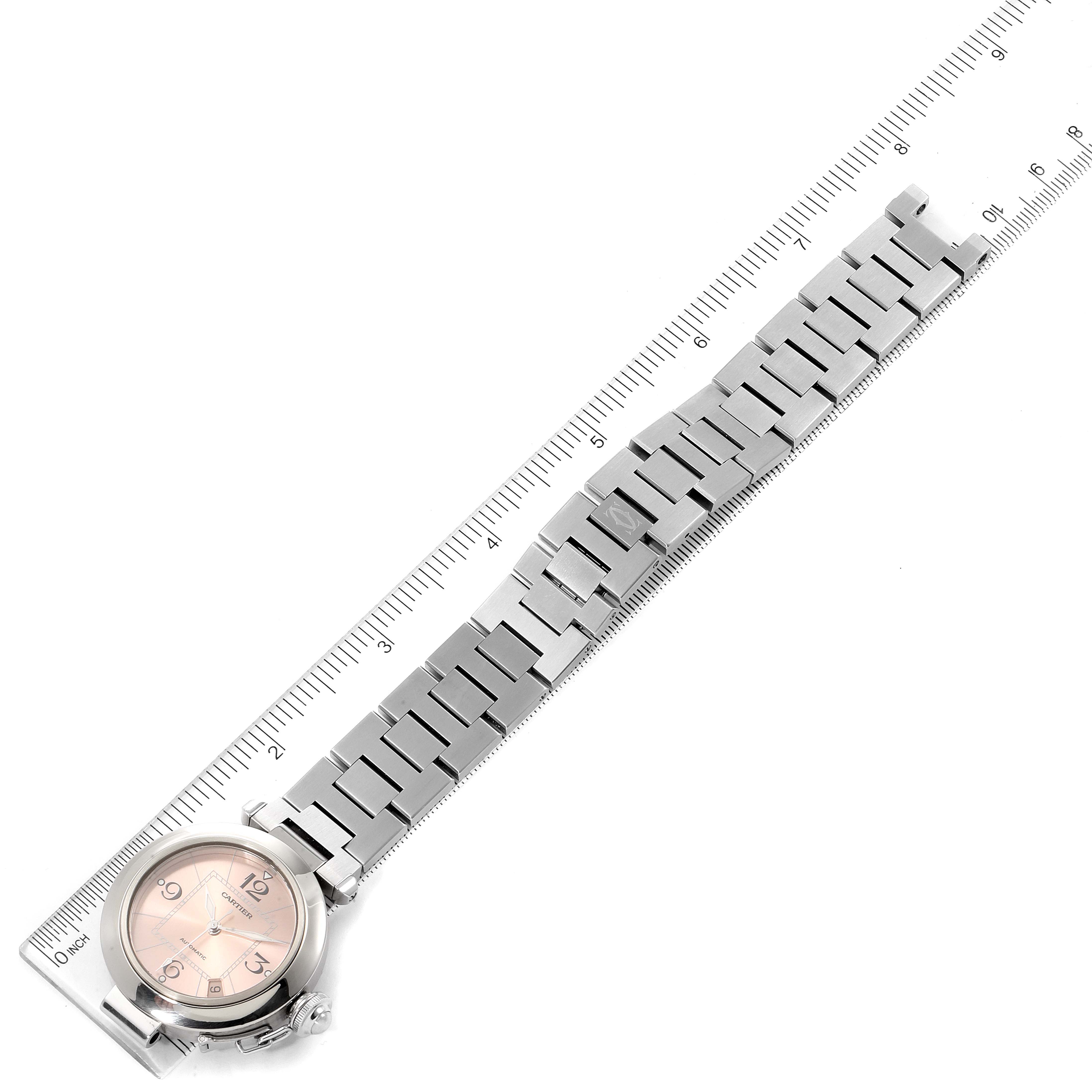 The image shows a Cartier Pasha W31075M7 Women's Stainless Steel Pink Dial W31075M7 Women's Stainless Steel Pink Dial watch laid flat along a ruler, displaying its face and metal bracelet.