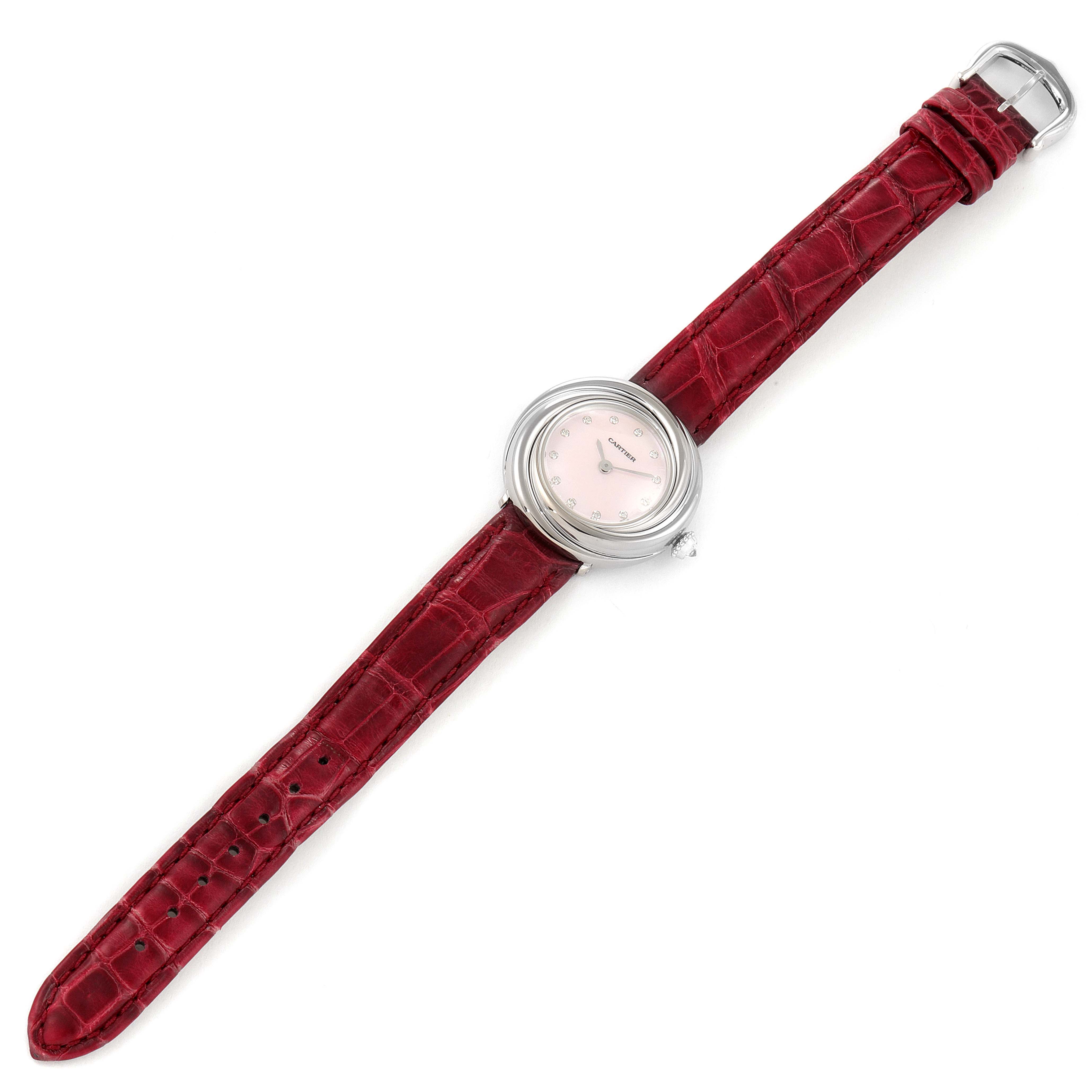 The Cartier Trinity WG200846 Women's White Gold Mother of Pearl Dial watch is shown from a top view, highlighting its round silver case, pink dial, and red leather strap.