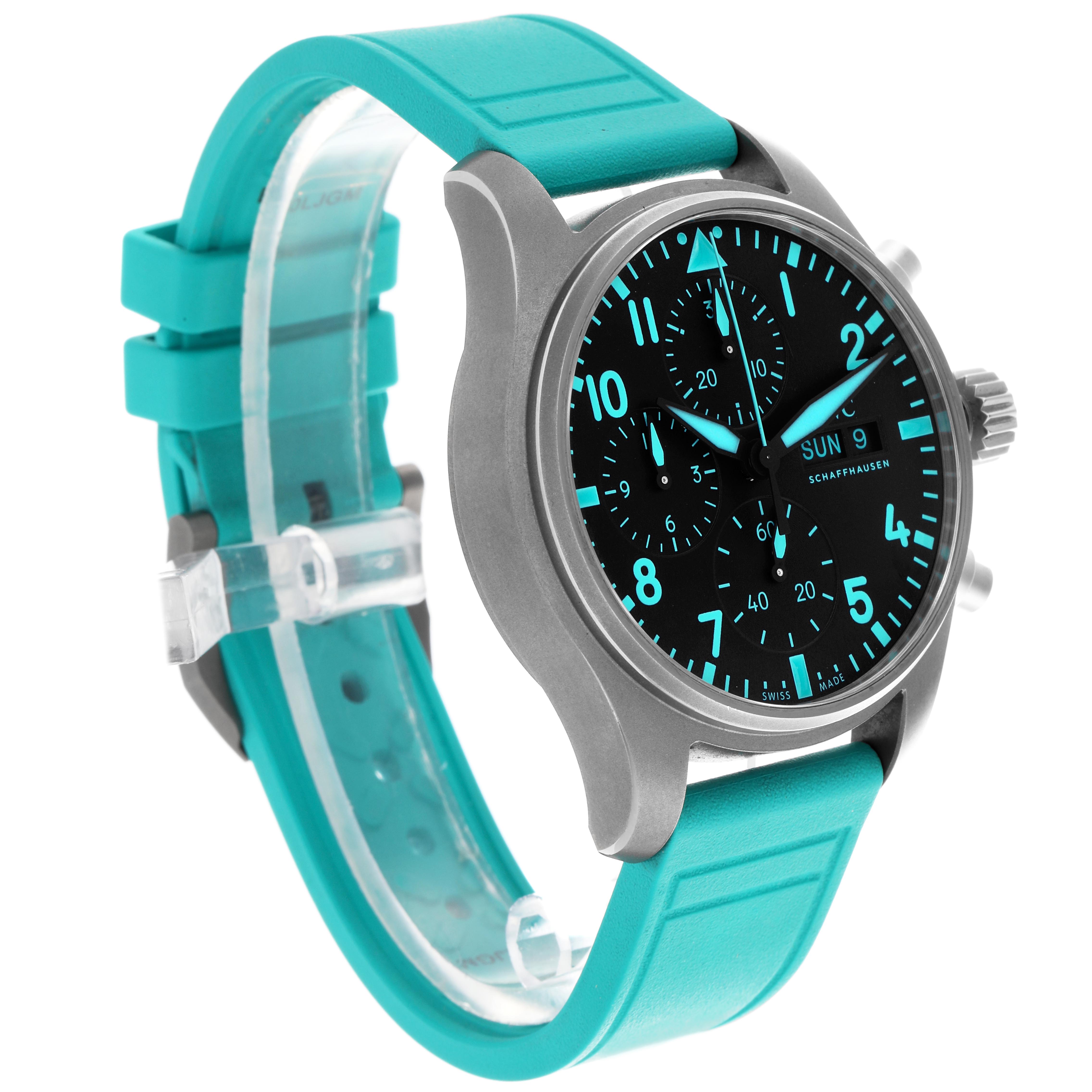 The IWC Pilot IW388108 Men's Titanium Black Dial watch is shown at an angled side view, highlighting the dial, crown, pushers, and blue strap.