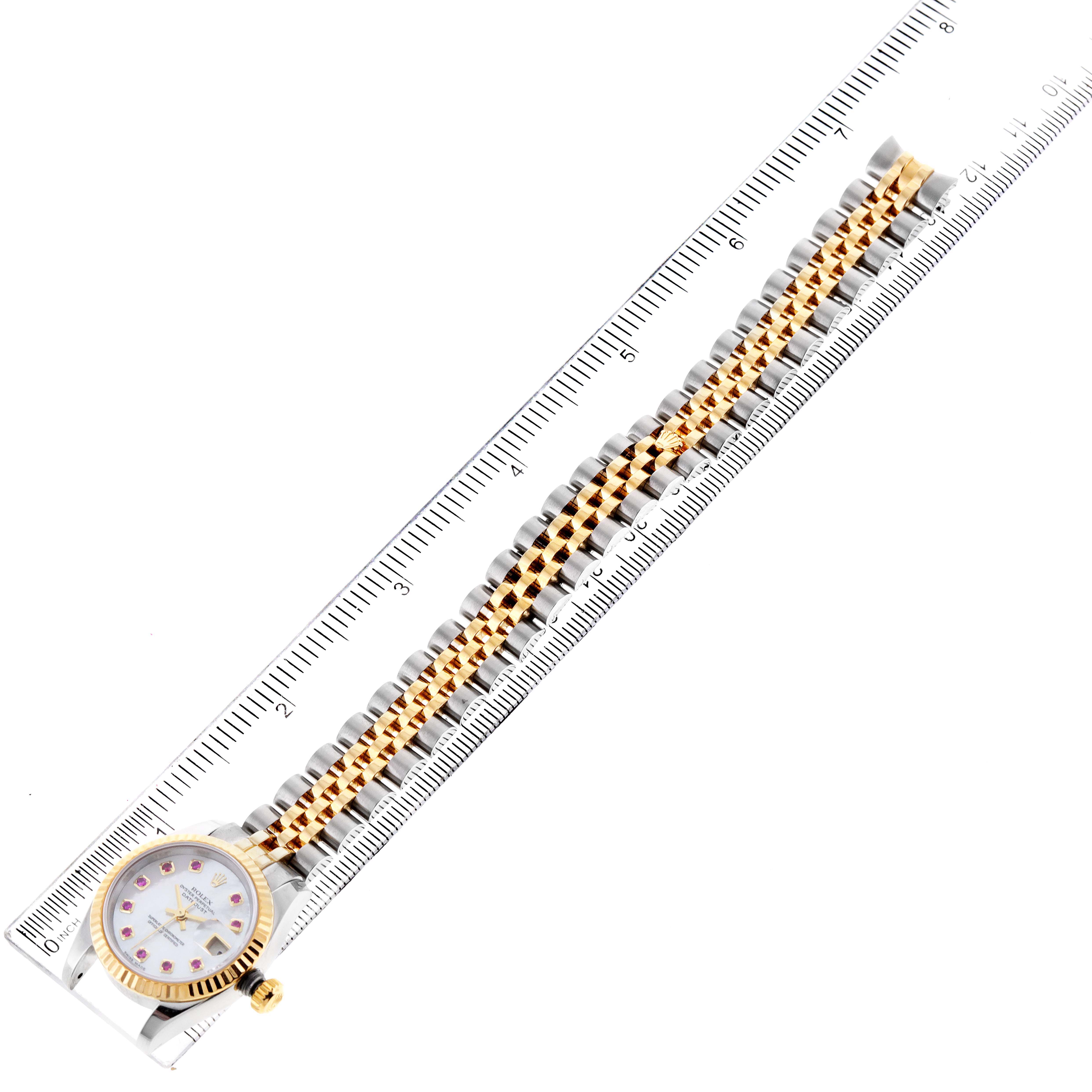 The Rolex Datejust 179173 Women's Steel and Gold (two tone) Mother of Pearl Dial 179173 Women's Steel and Gold (two tone) Mother of Pearl Dial watch is shown from a top-down angle, displaying its face, crown, and two-tone bracelet next to a ruler.