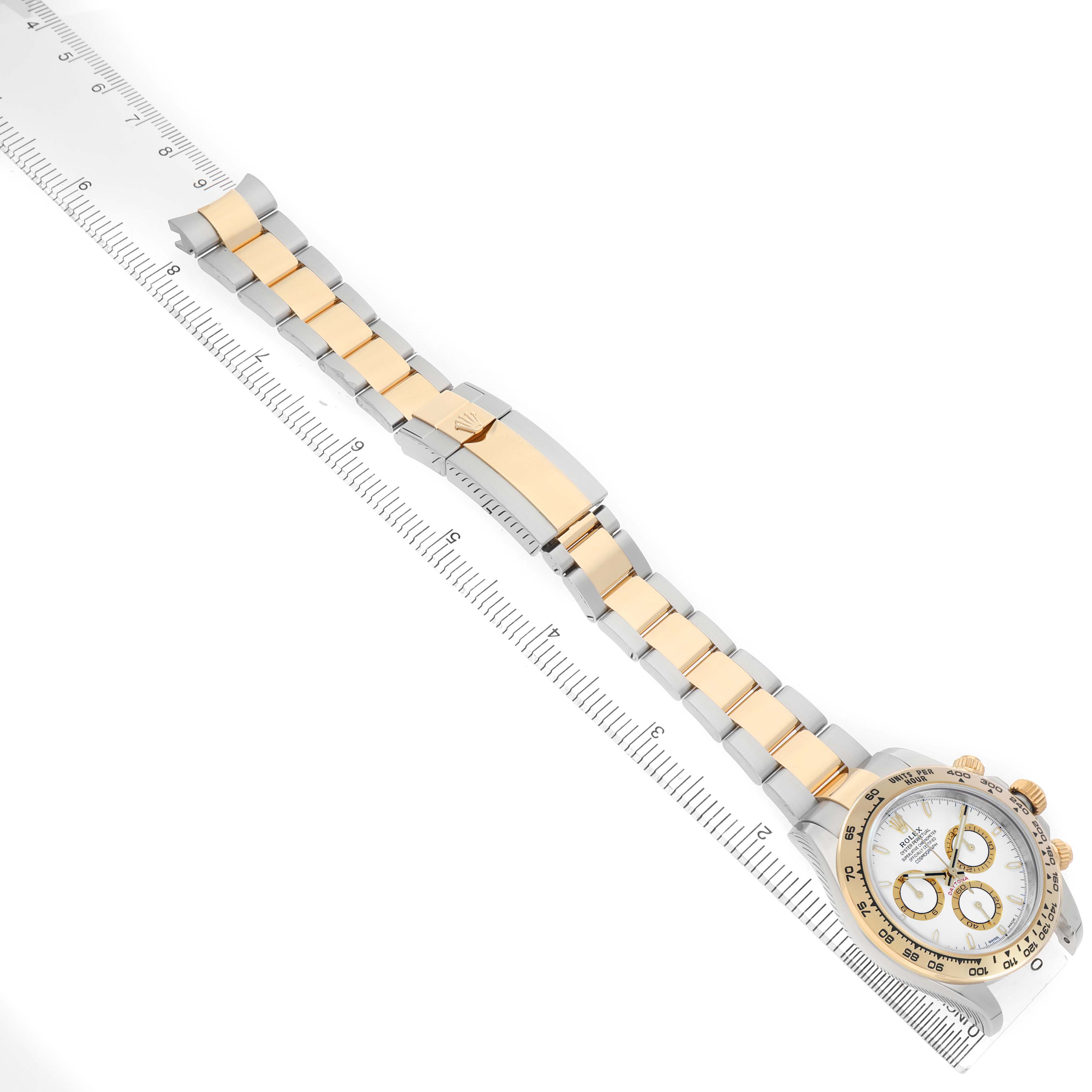 The Rolex Daytona M126503-0001 Men's Steel and Gold (two tone) White Dial watch is shown at a diagonal angle, featuring the bracelet, clasp, and watch face alongside a ruler for scale.