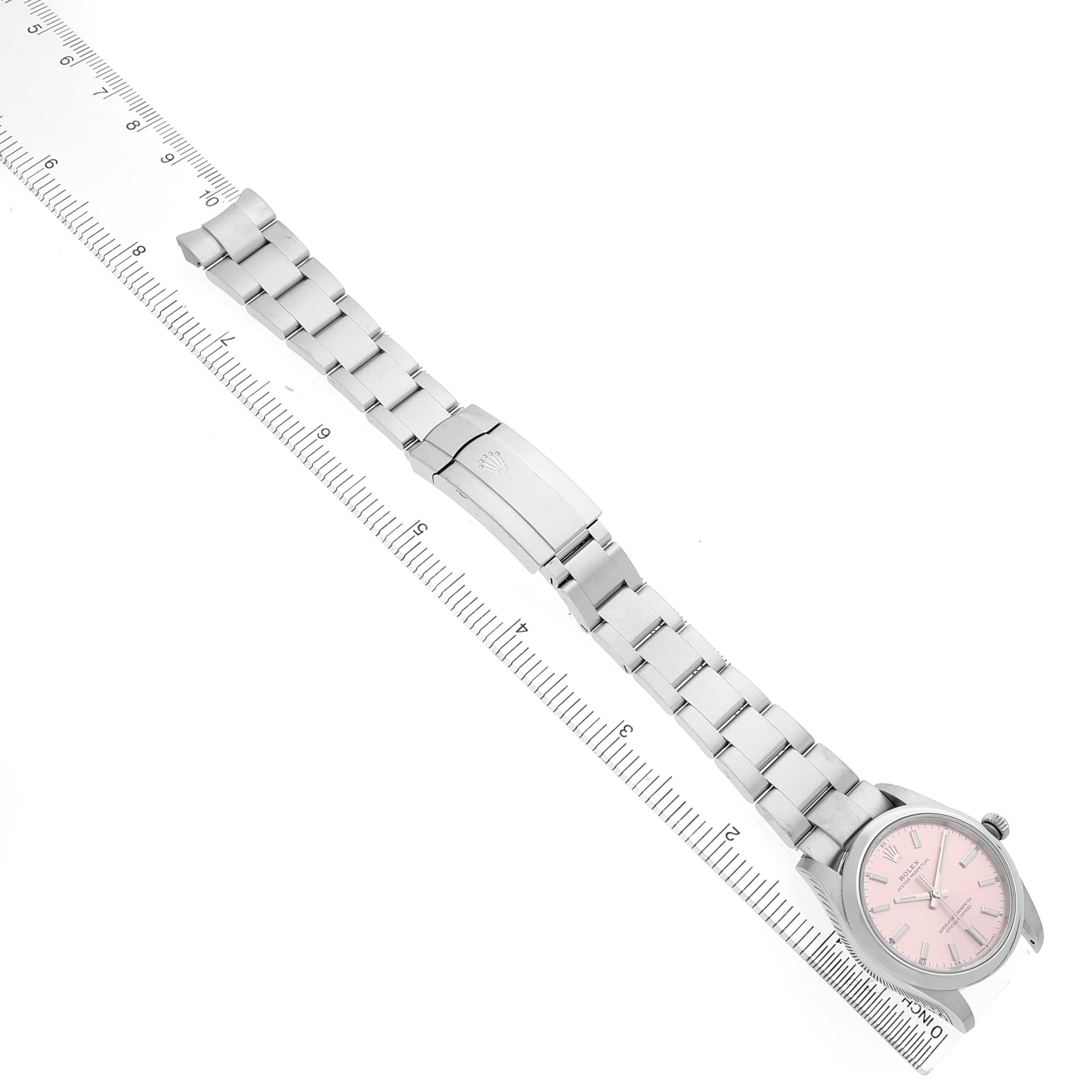 The Rolex Oyster Perpetual 124200 Men's Stainless Steel Pink Dial watch is shown from an overhead angle, displaying the full band, clasp, and pink dial on a ruler.