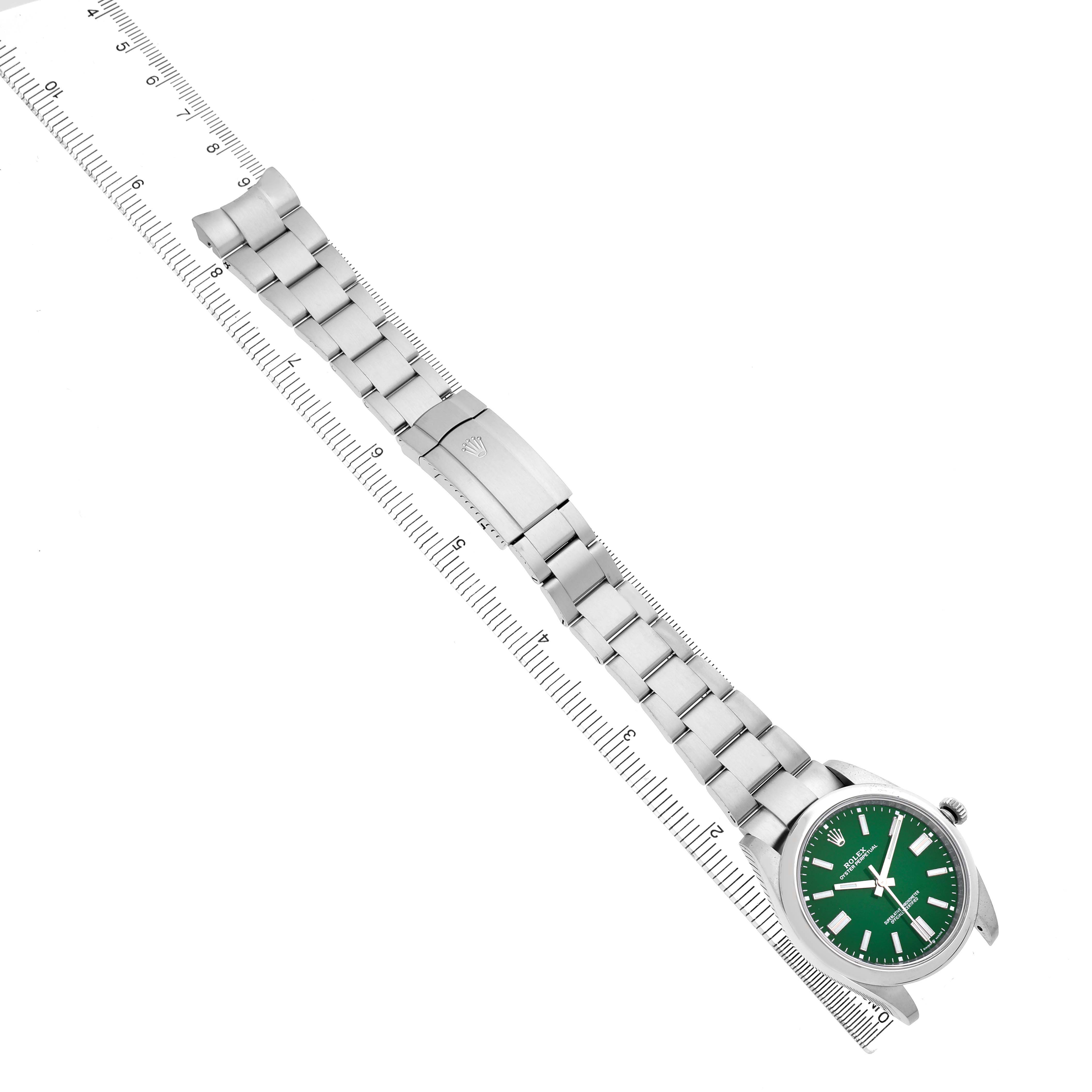 The image shows a top view of a Rolex Oyster Perpetual 124300 Men's Stainless Steel Green Dial watch with a green dial and metal bracelet alongside a ruler.