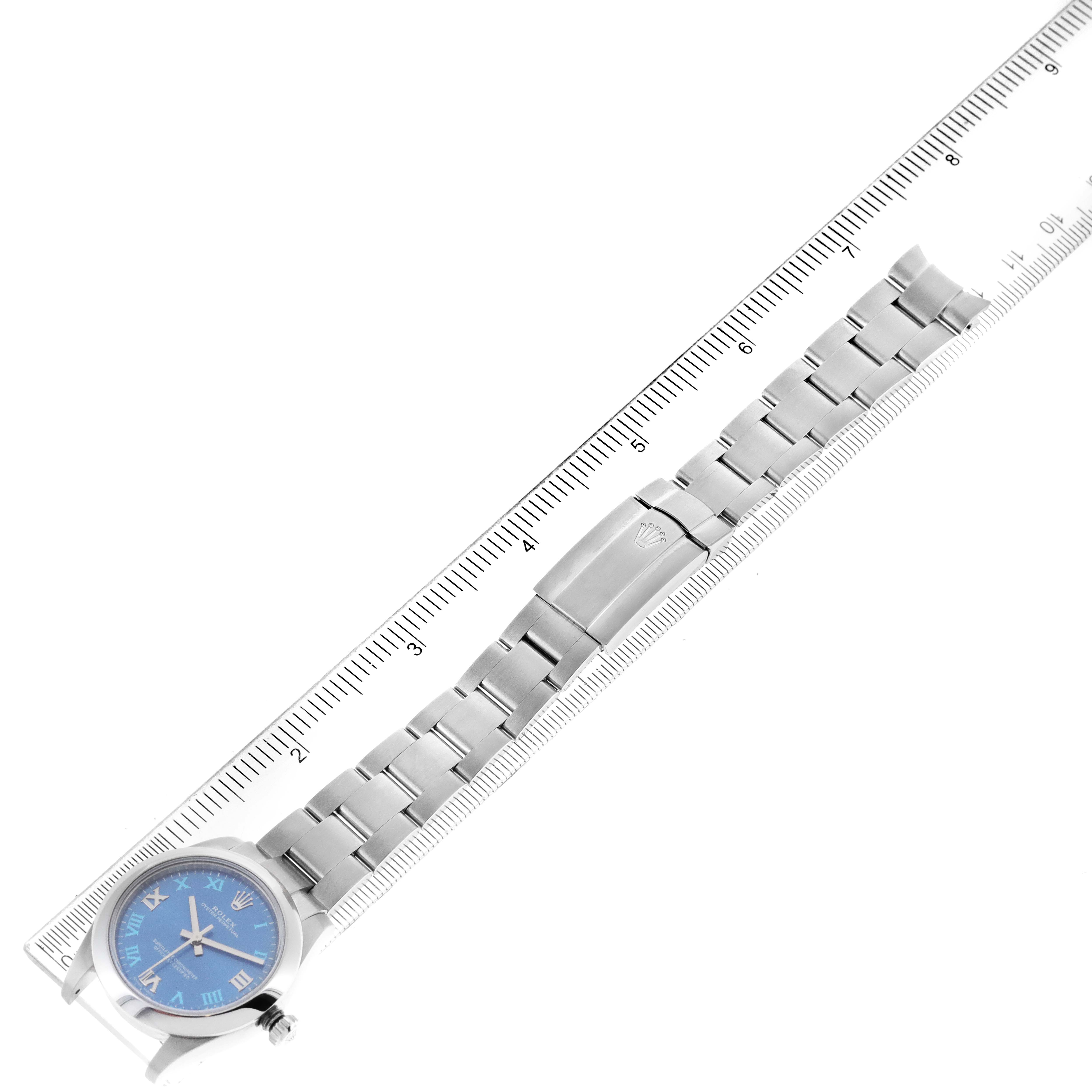 The image shows a top-down view of a Rolex Mid-Size 177200 Women
s Stainless Steel Blue Dial 177200 Women
s Stainless Steel Blue Dial watch with a blue dial and metal bracelet next to a ruler.