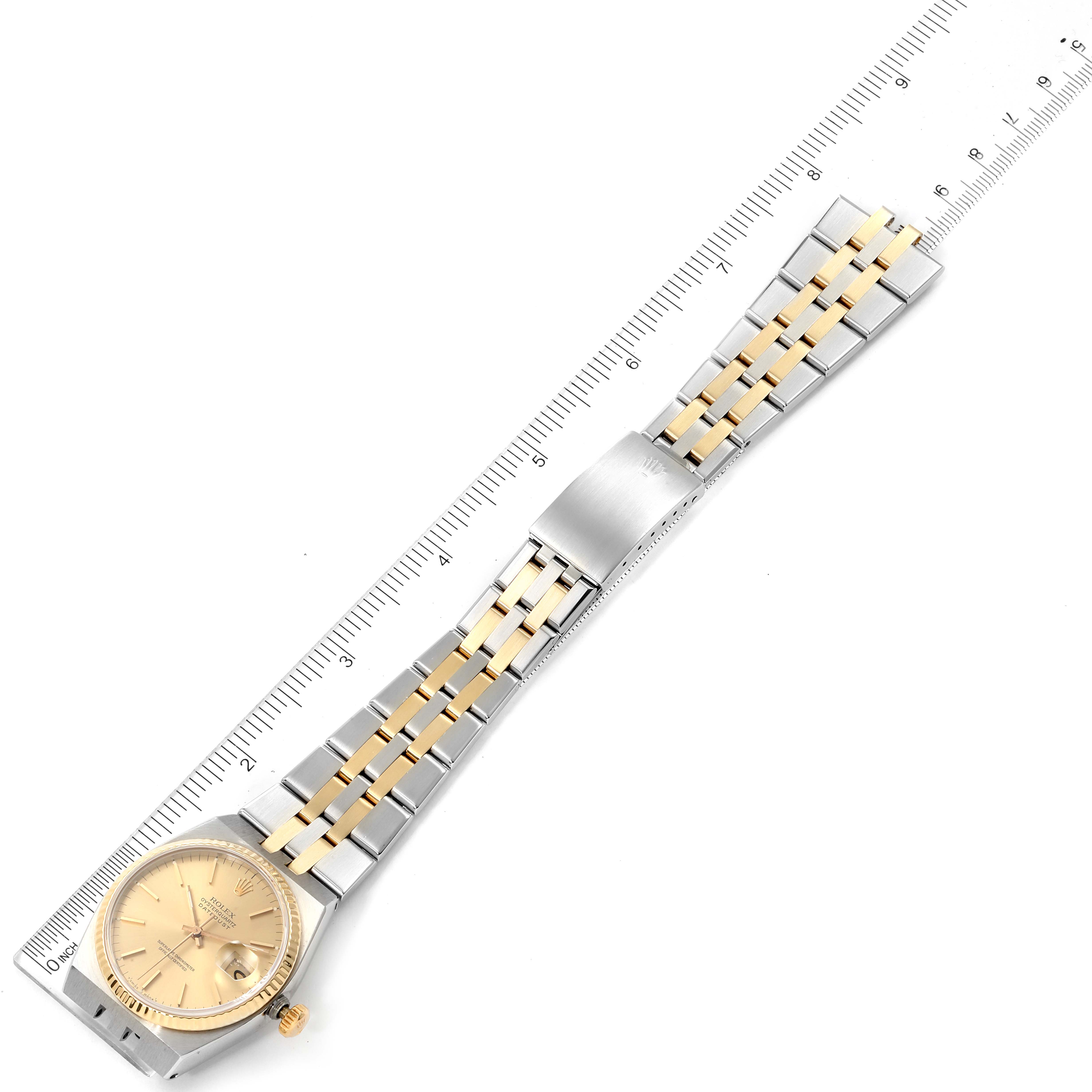 The Rolex Oysterquartz 17013 Men's Steel and Gold (two tone) Champagne Dial 17013 Men's Steel and Gold (two tone) Champagne Dial watch is shown flat with a gold and silver bracelet alongside a ruler for scale.