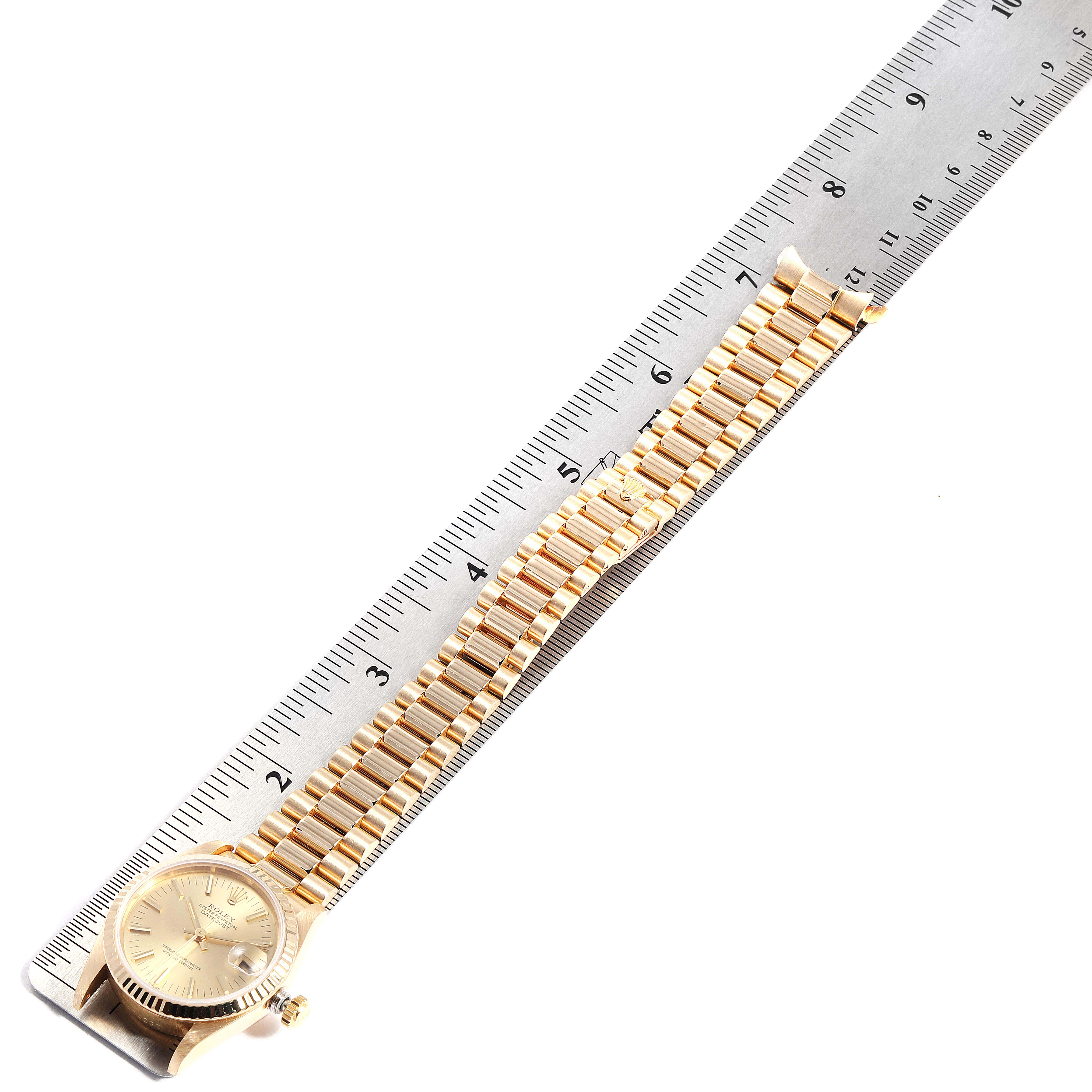 The Rolex President 68278 Women
s Yellow Gold Champagne Dial 68278 Women
s Yellow Gold Champagne Dial model watch is shown from an overhead angle, displaying its face and full bracelet alongside a ruler.
