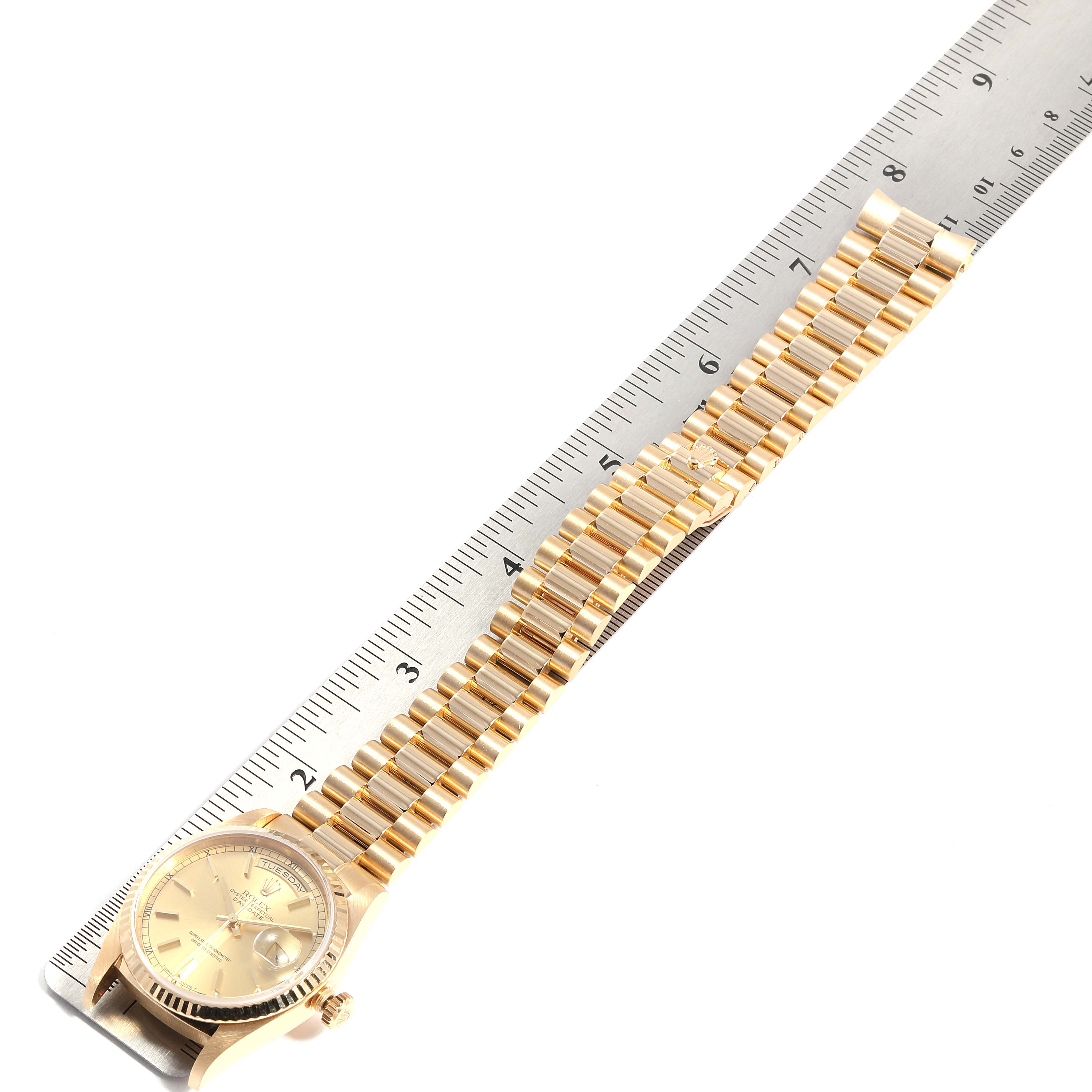 The image shows a top-down view of a Rolex President 18238 Men
s Yellow Gold Champagne Dial 18238 Men
s Yellow Gold Champagne Dial watch with its golden bracelet placed alongside a ruler.