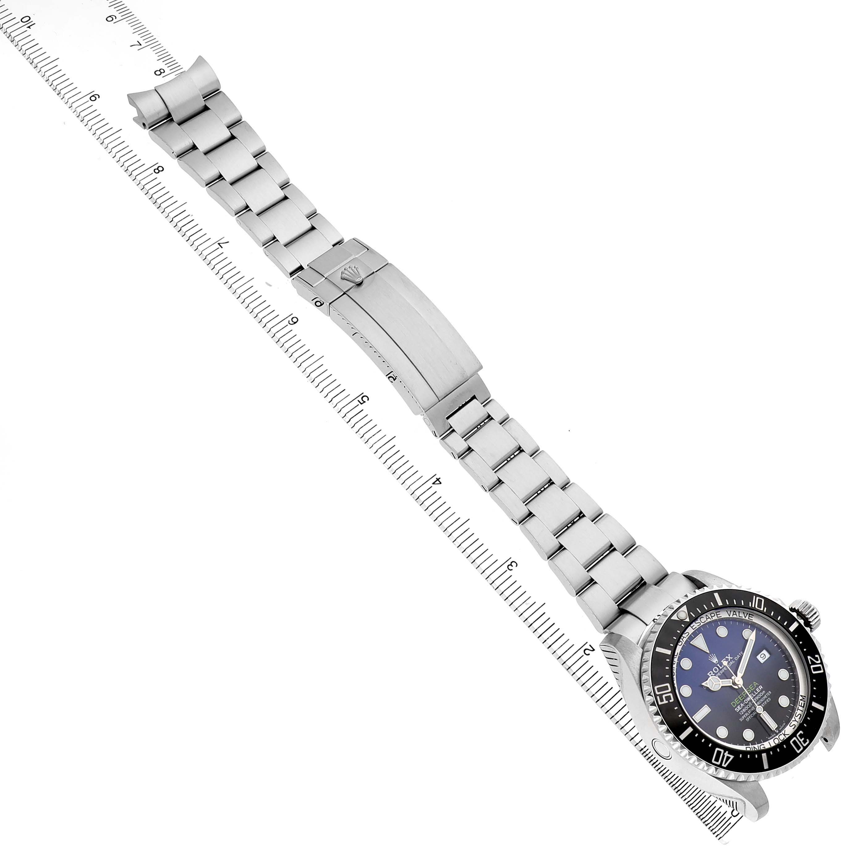 The Rolex Sea-Dweller 126660 Men's Stainless Steel Blue Dial watch is shown from an angled top view, displaying the bracelet, clasp, and watch face with a ruler alongside.