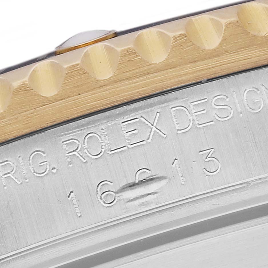 This image shows a close-up of the bezel and part of the case of a Rolex Submariner 16613 Men's Steel and Gold (two tone) Black Dial 16613 Men's Steel and Gold (two tone) Black Dial watch, featuring engraving details.