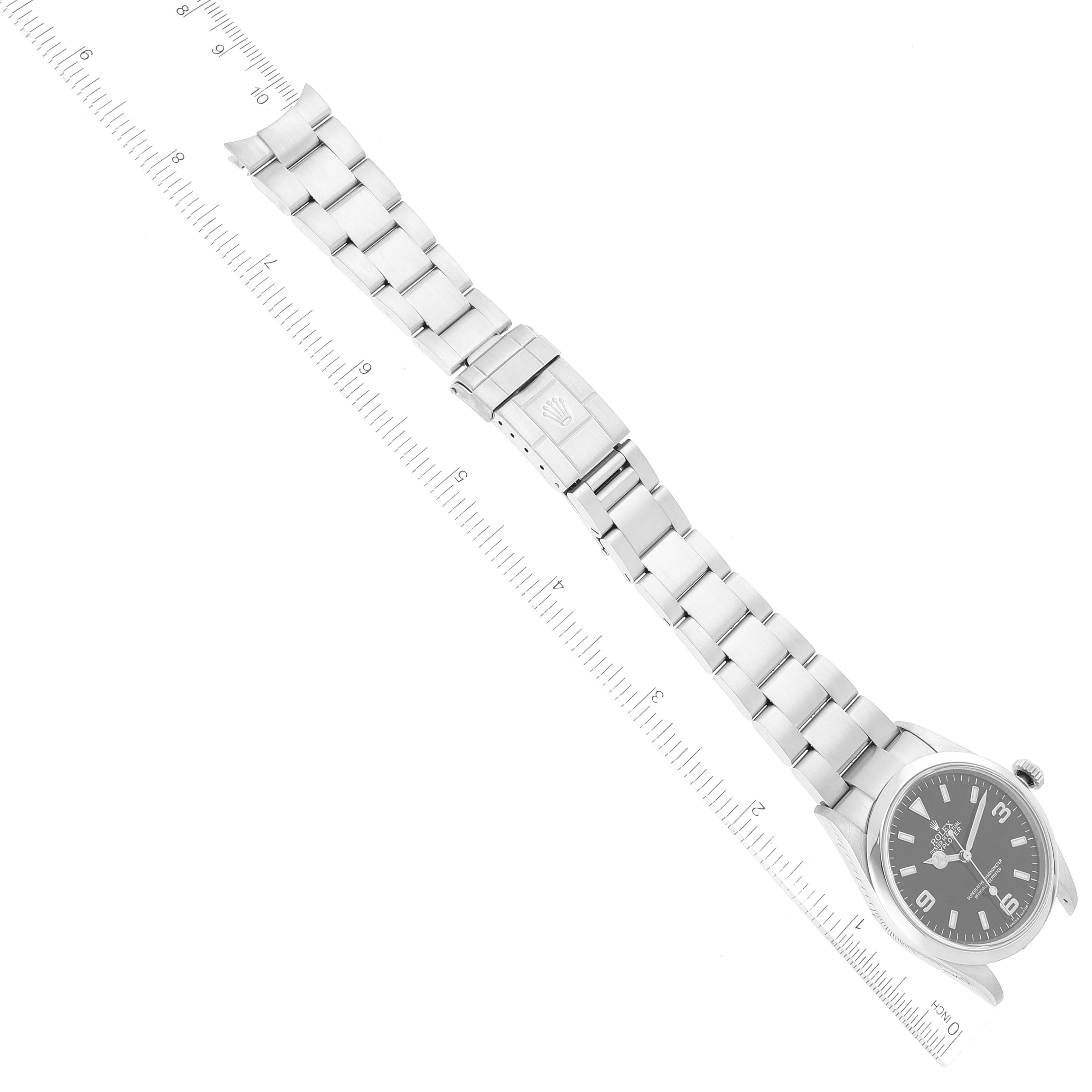 The image shows an overhead view of a Rolex Explorer 114270 Men
s Stainless Steel Black Dial 114270 Men
s Stainless Steel Black Dial watch with its full metal band and a ruler for scale.