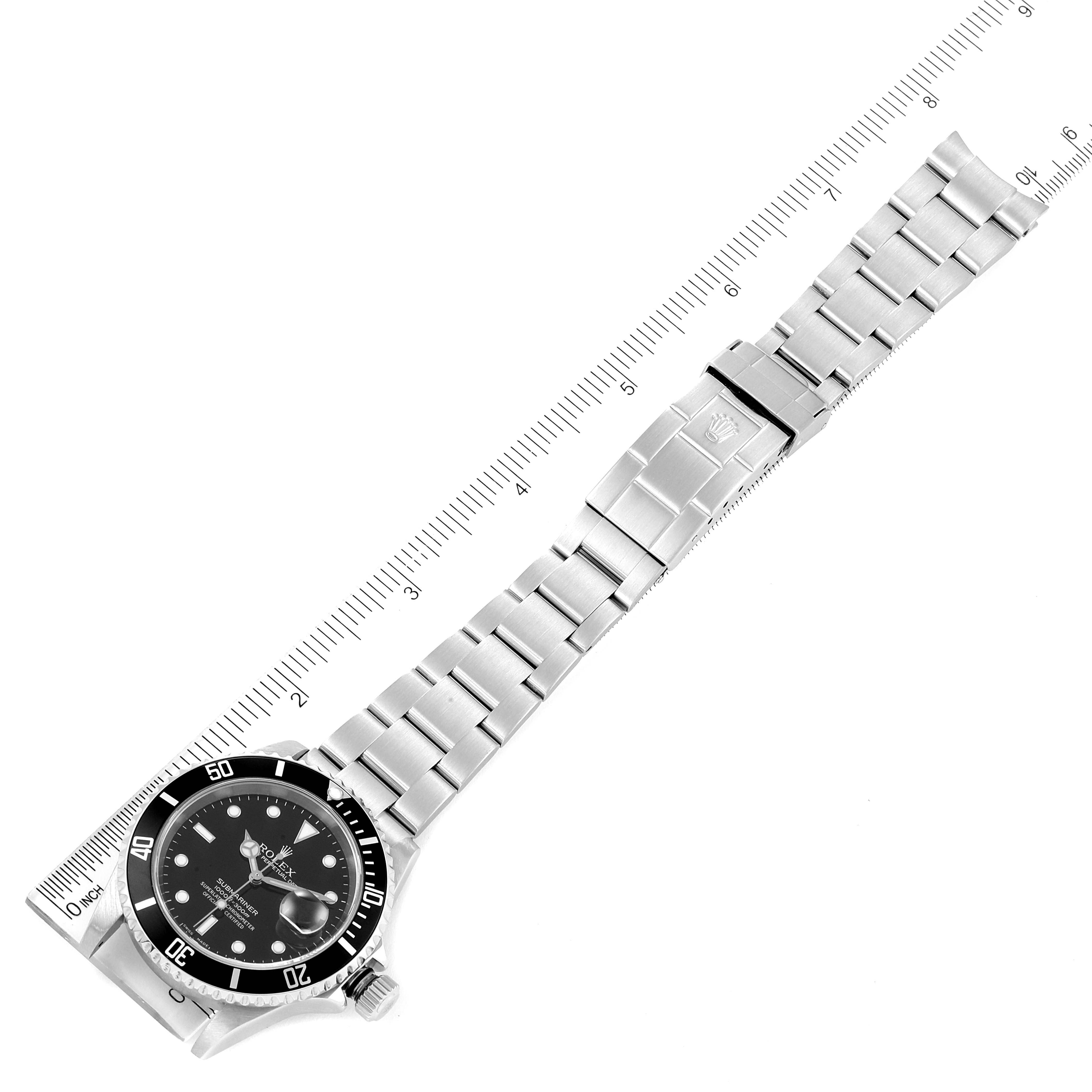 This image displays a Rolex Submariner 16610 Men
s Stainless Steel Black Dial 16610 Men
s Stainless Steel Black Dial watch laid flat, showing its face, bracelet, and clasp next to a ruler for measurement.