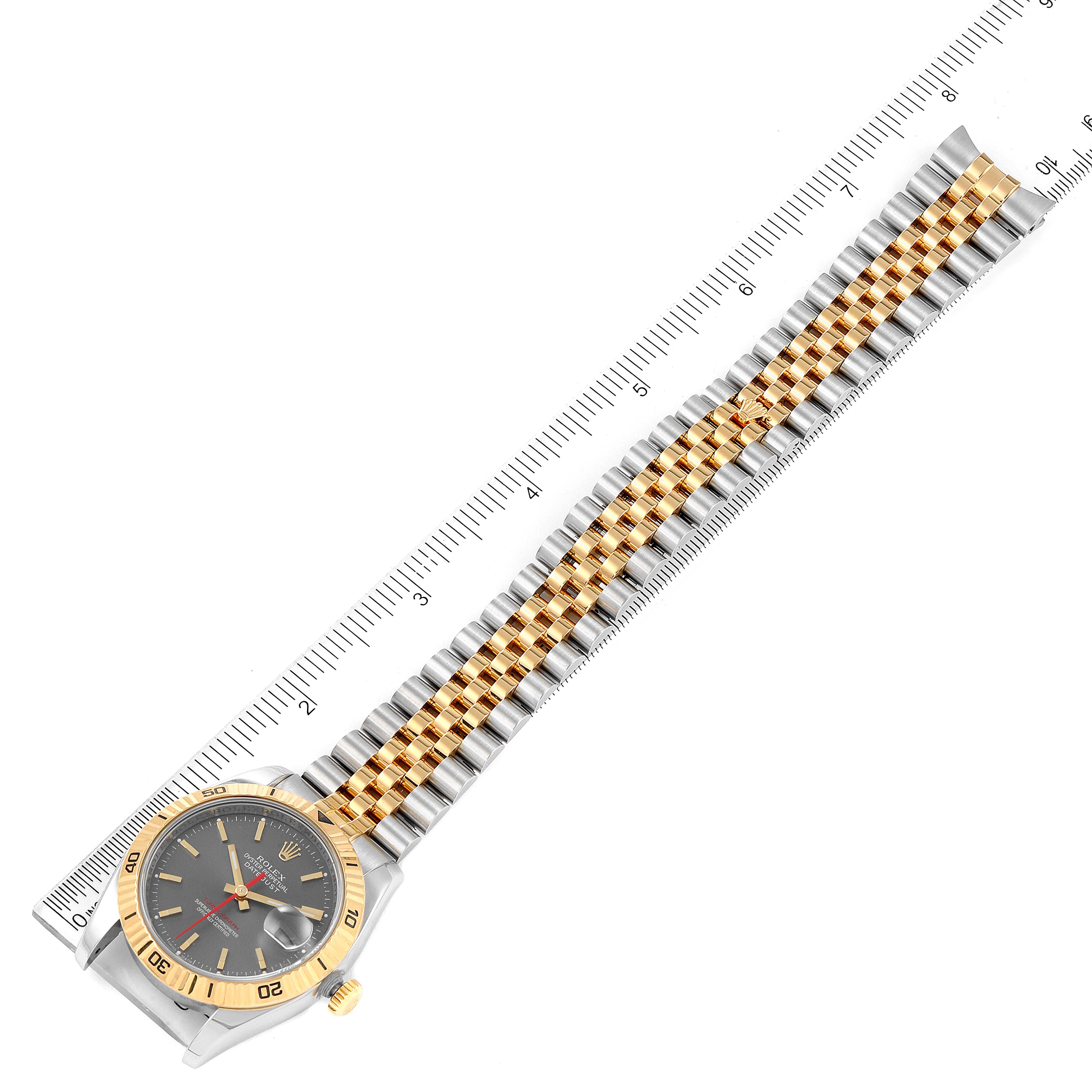 The Rolex Turn-o-Graph 116263 Men
s Steel and Gold (two tone) Grey Dial 116263 Men
s Steel and Gold (two tone) Grey Dial watch is shown from a top-down angle, displaying the face, bezel, and entire bracelet against a ruler.
