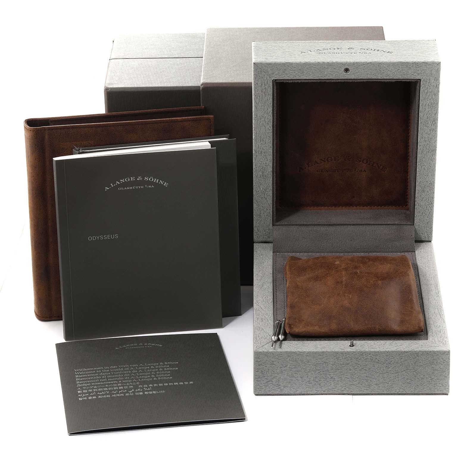 The image shows the packaging, leather case, manuals, and booklets for the Odysseus model by A. Lange & Söhne at an angle.