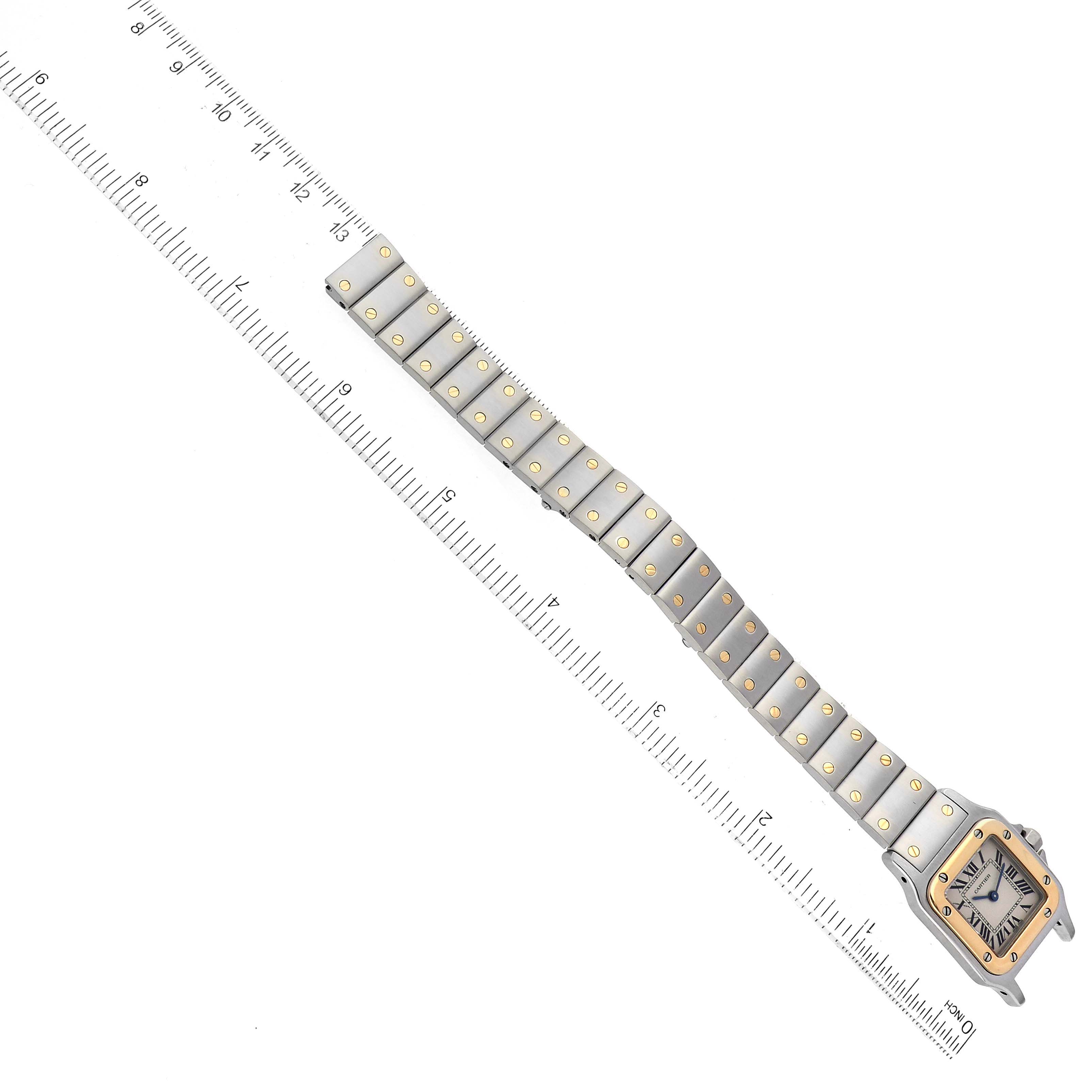 The Cartier Santos W20012C4 Women's Steel and Gold (two tone) Silver Dial W20012C4 Women's Steel and Gold (two tone) Silver Dial watch is laid flat with the face and entire metal band visible, alongside a measuring ruler.