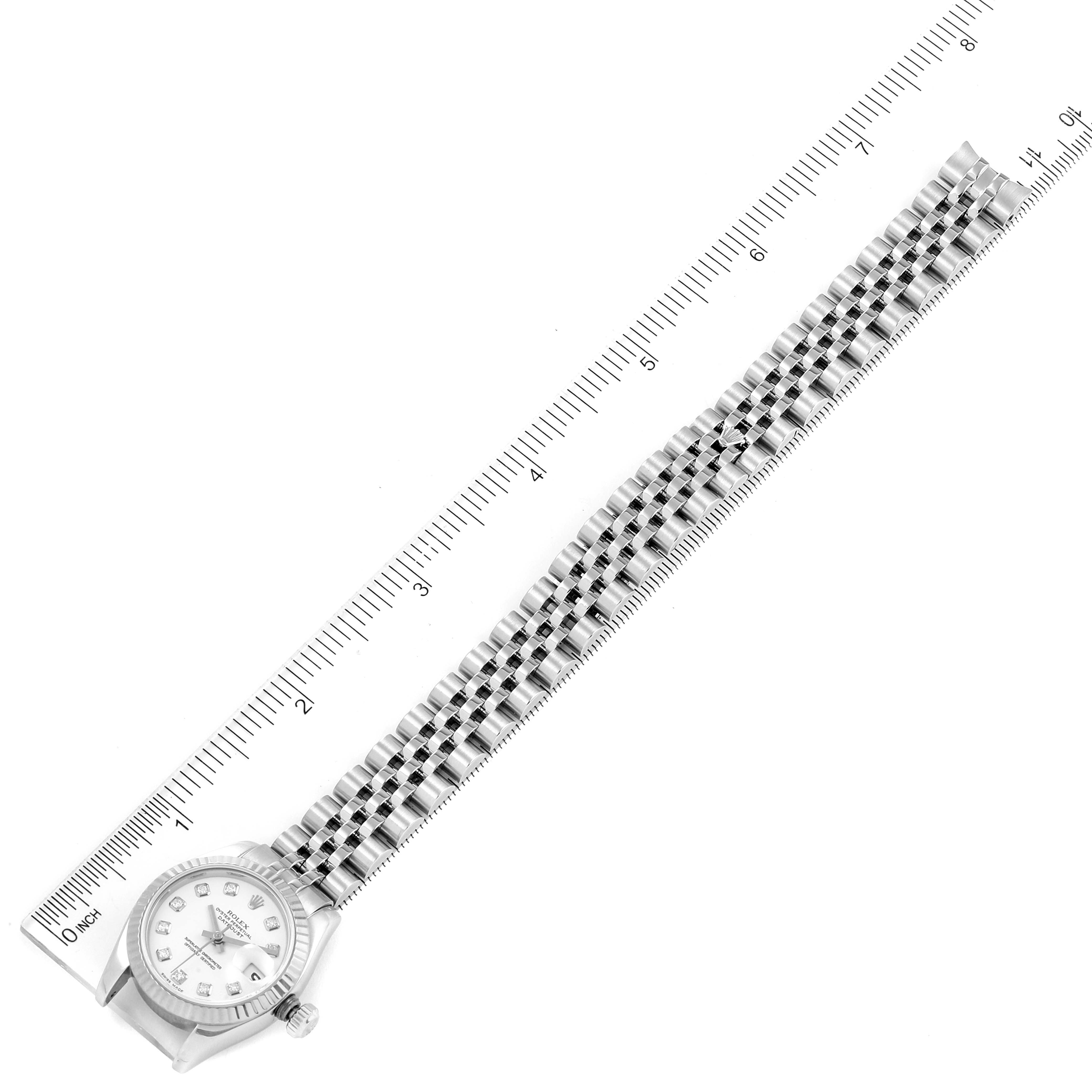 The image shows a top-down view of a Rolex Datejust 179174 Women's Stainless Steel White Dial 179174 Women's Stainless Steel White Dial watch with a full stainless steel bracelet placed alongside a ruler.