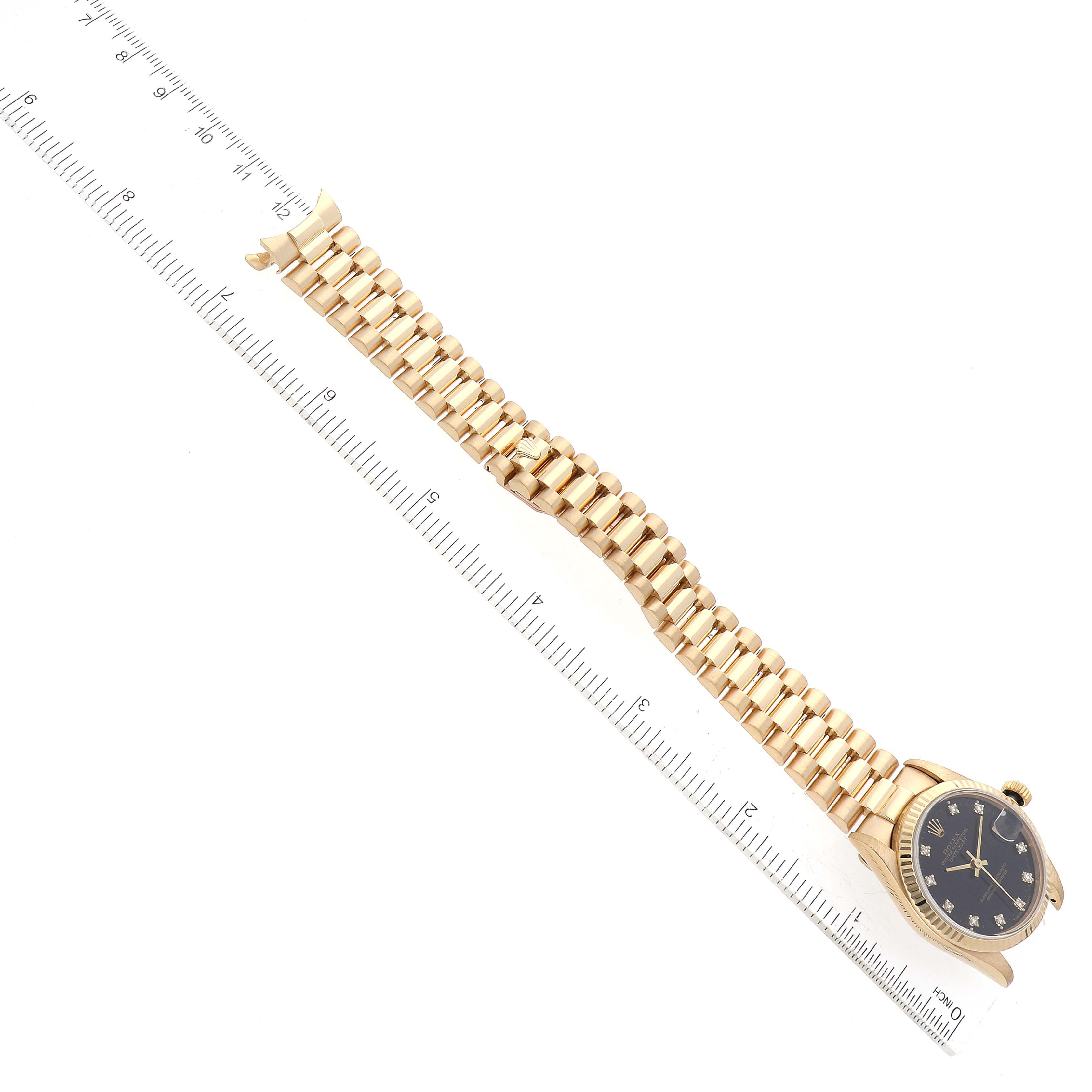 The image shows a Rolex President 68278G Women's Yellow Gold Black Dial 68278G Women's Yellow Gold Black Dial model watch laid flat, showcasing its gold bracelet and black dial, aligned beside a ruler.