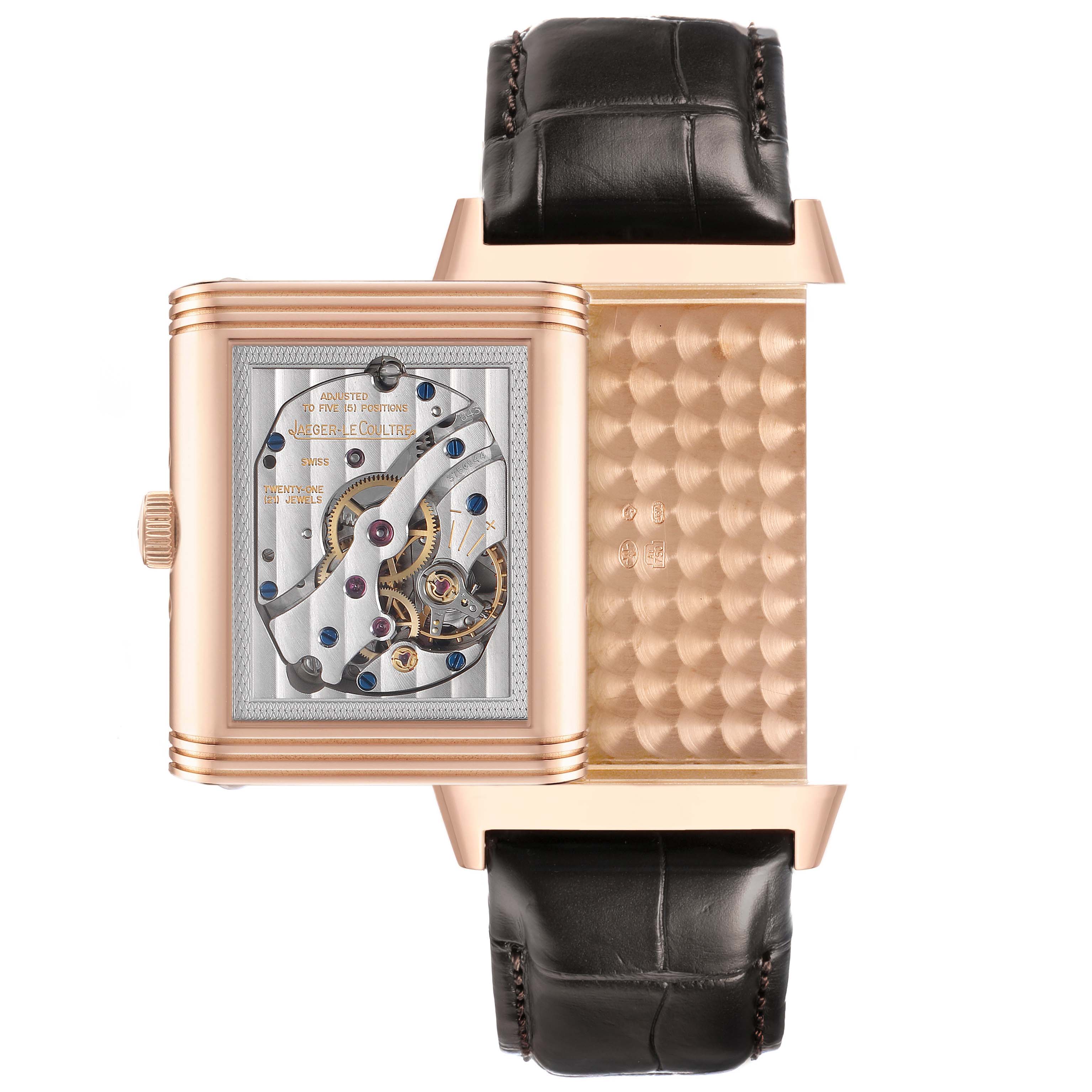 The Jaeger-LeCoultre Reverso watch is shown in an open position, revealing the movement and intricate case interior.