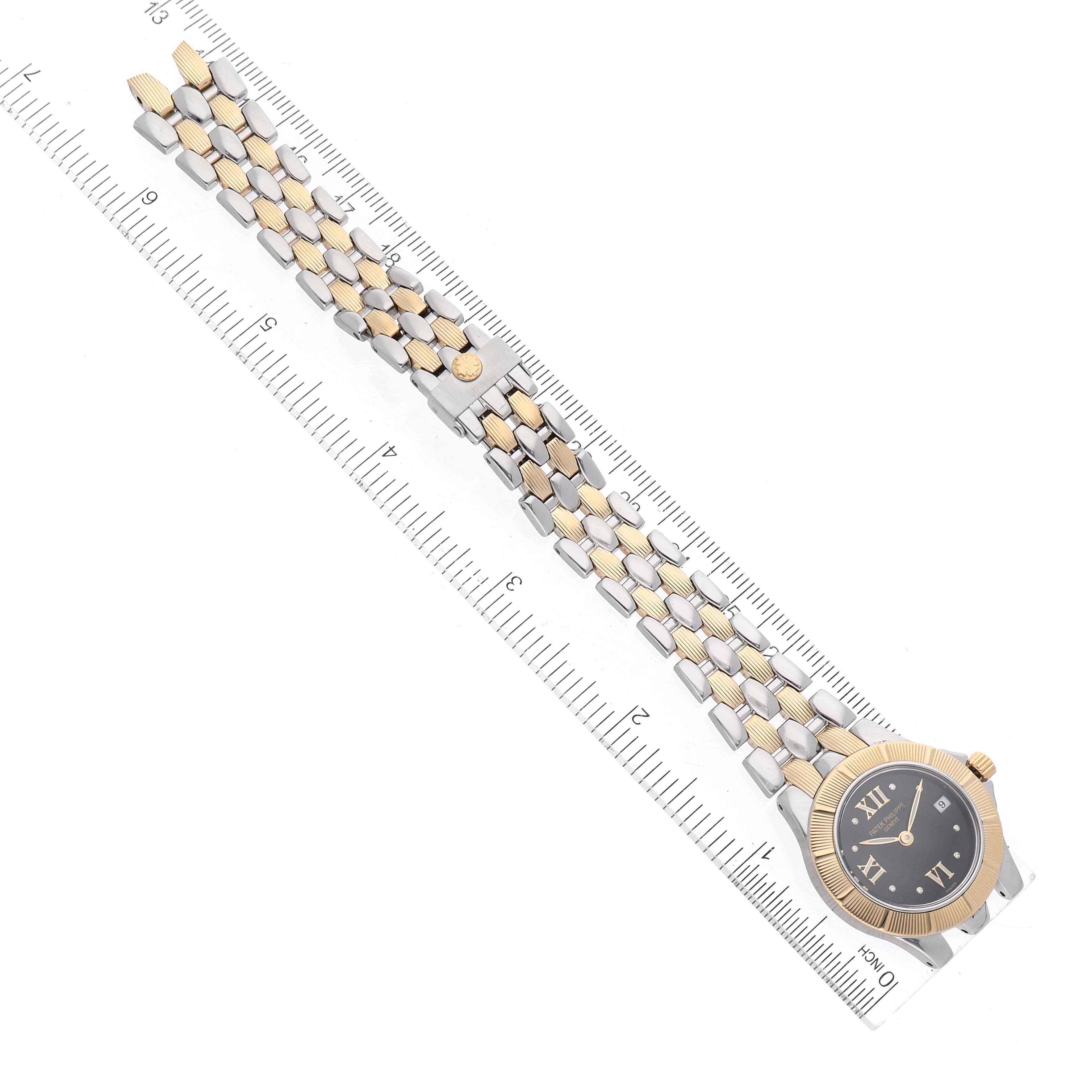 The Patek Philippe Neptune 4880/1JA Women's Steel and Gold (two tone) Black Dial watch is shown from a top-down angle, highlighting its two-tone bracelet and face against a ruler backdrop.