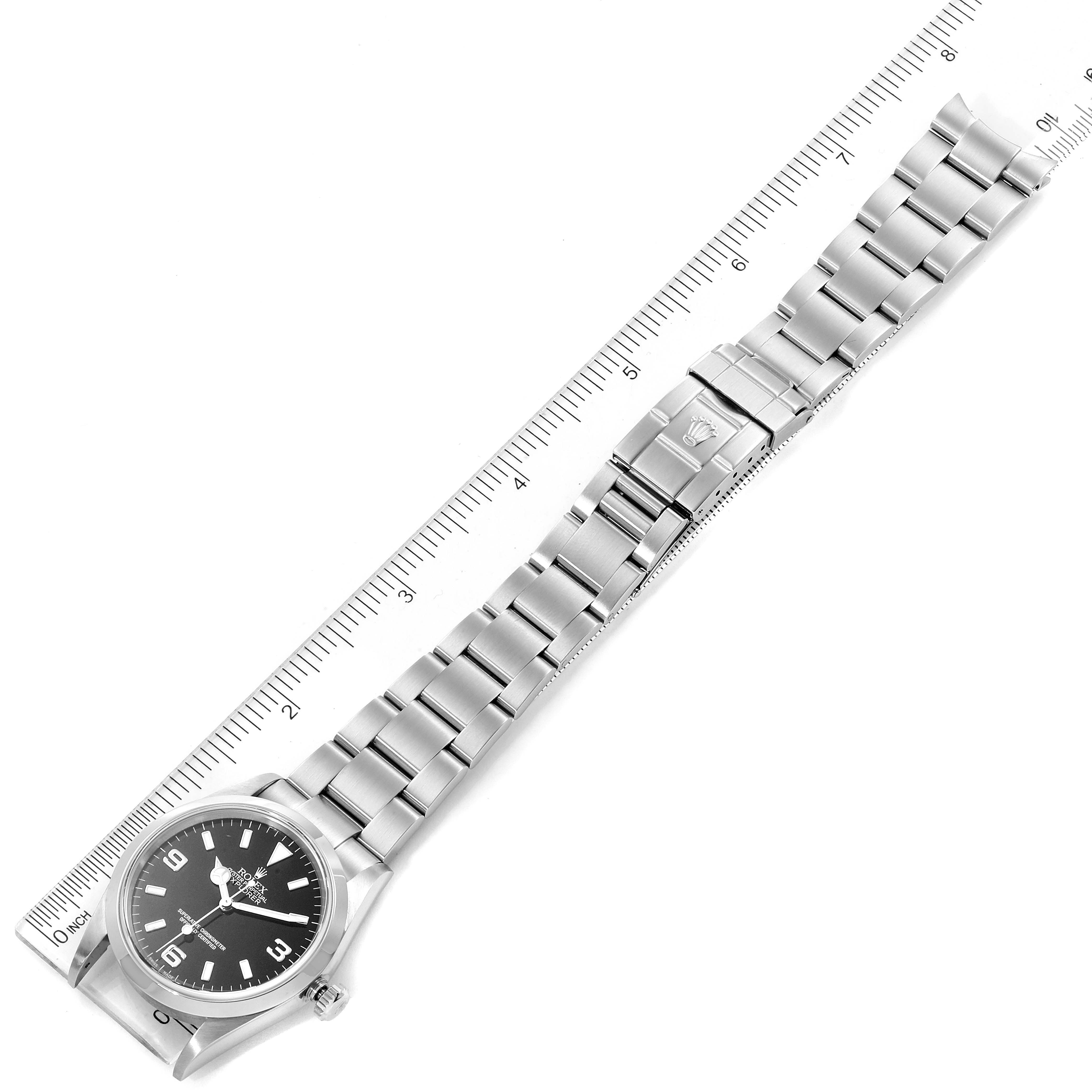 The image displays a top-down view of a Rolex Explorer 114270 Men
s Stainless Steel Black Dial 114270 Men
s Stainless Steel Black Dial watch alongside a ruler for size reference, highlighting the watch
s bracelet and clasp.