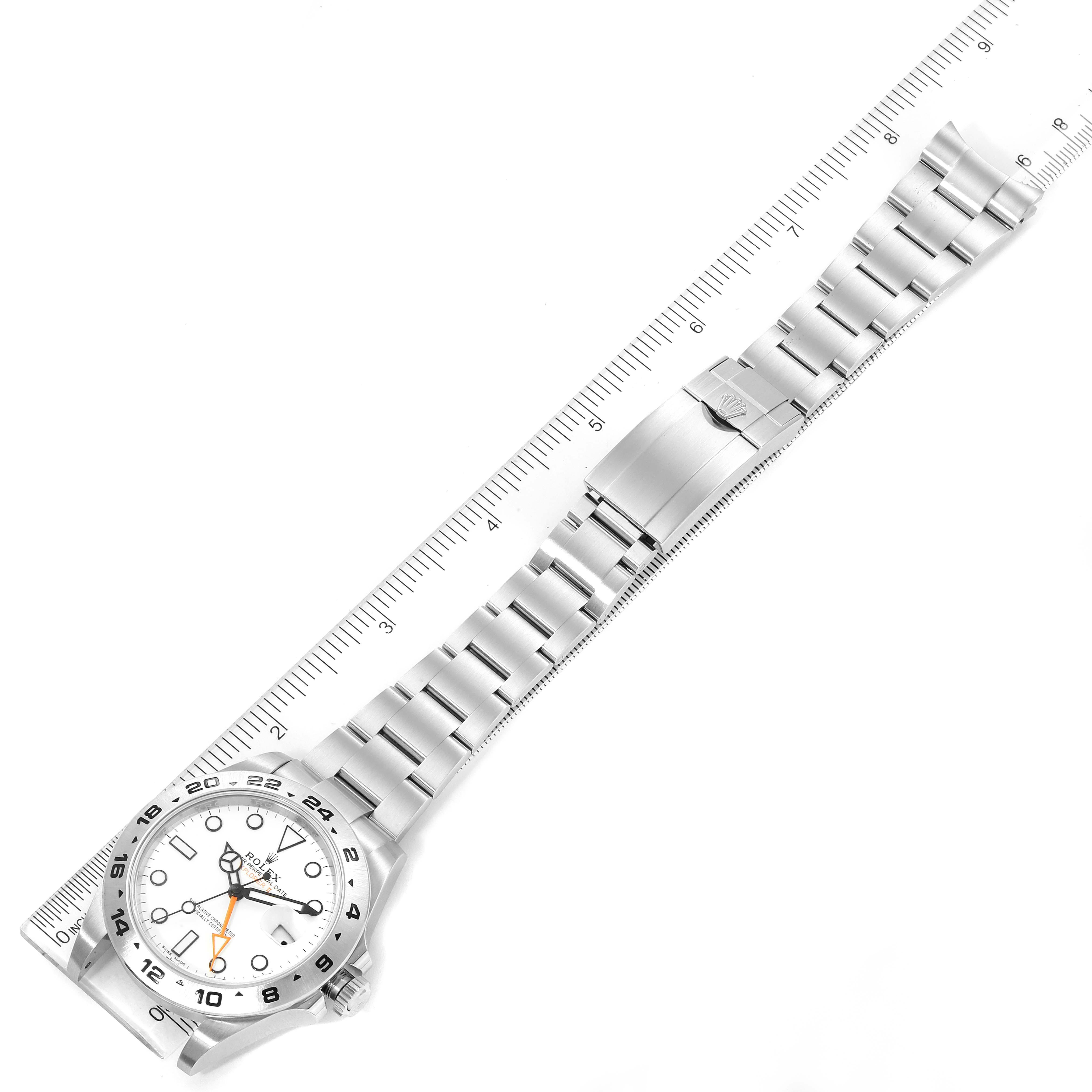 The image shows a top-down view of a Rolex Explorer 216570 Men
s Stainless Steel White Dial 216570 Men
s Stainless Steel White Dial watch with its full bracelet and clasp laid alongside a ruler.