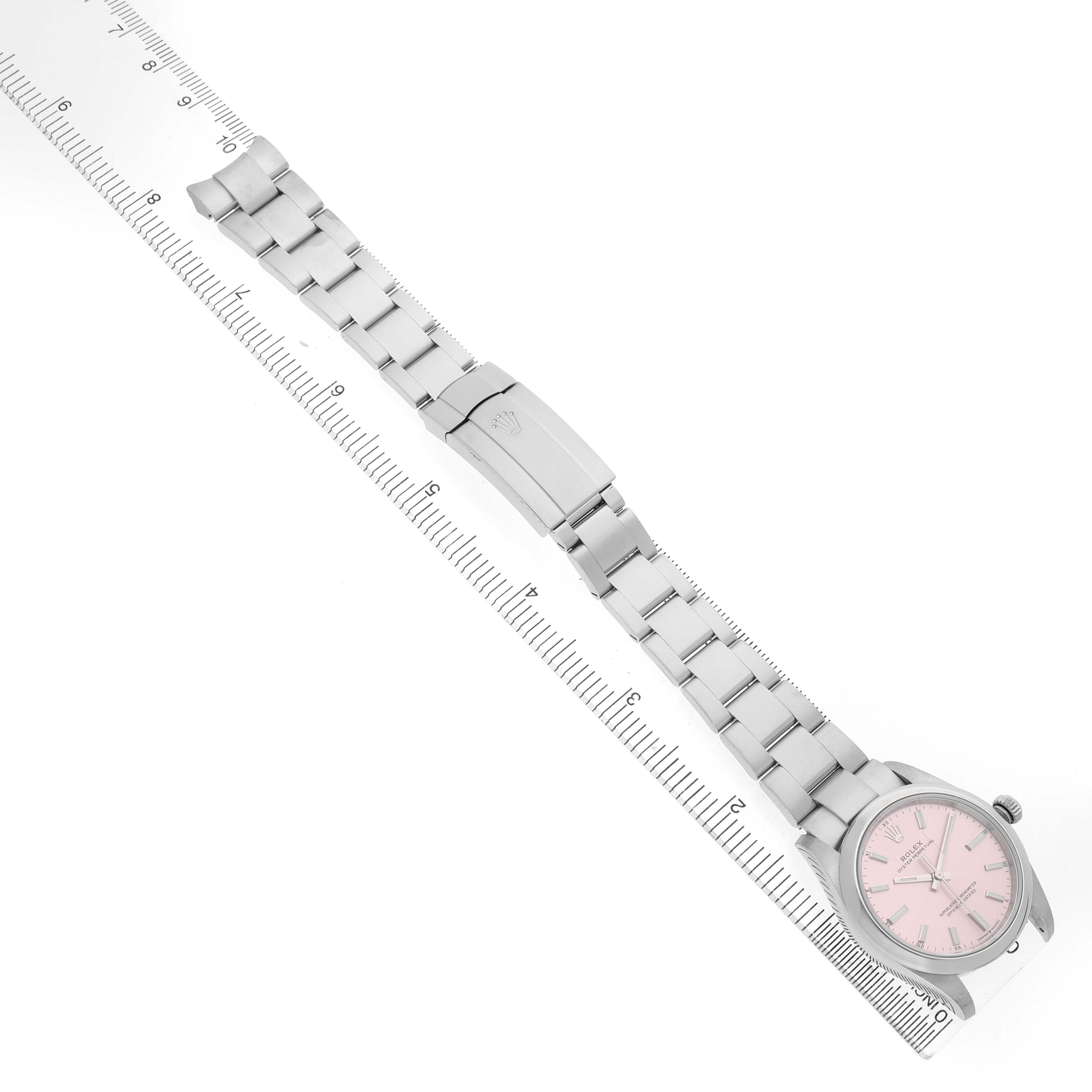 The Rolex Oyster Perpetual 124200 Women's Stainless Steel Pink Dial watch is shown from a top-down angle displaying the bracelet, clasp, and pink dial alongside a ruler.