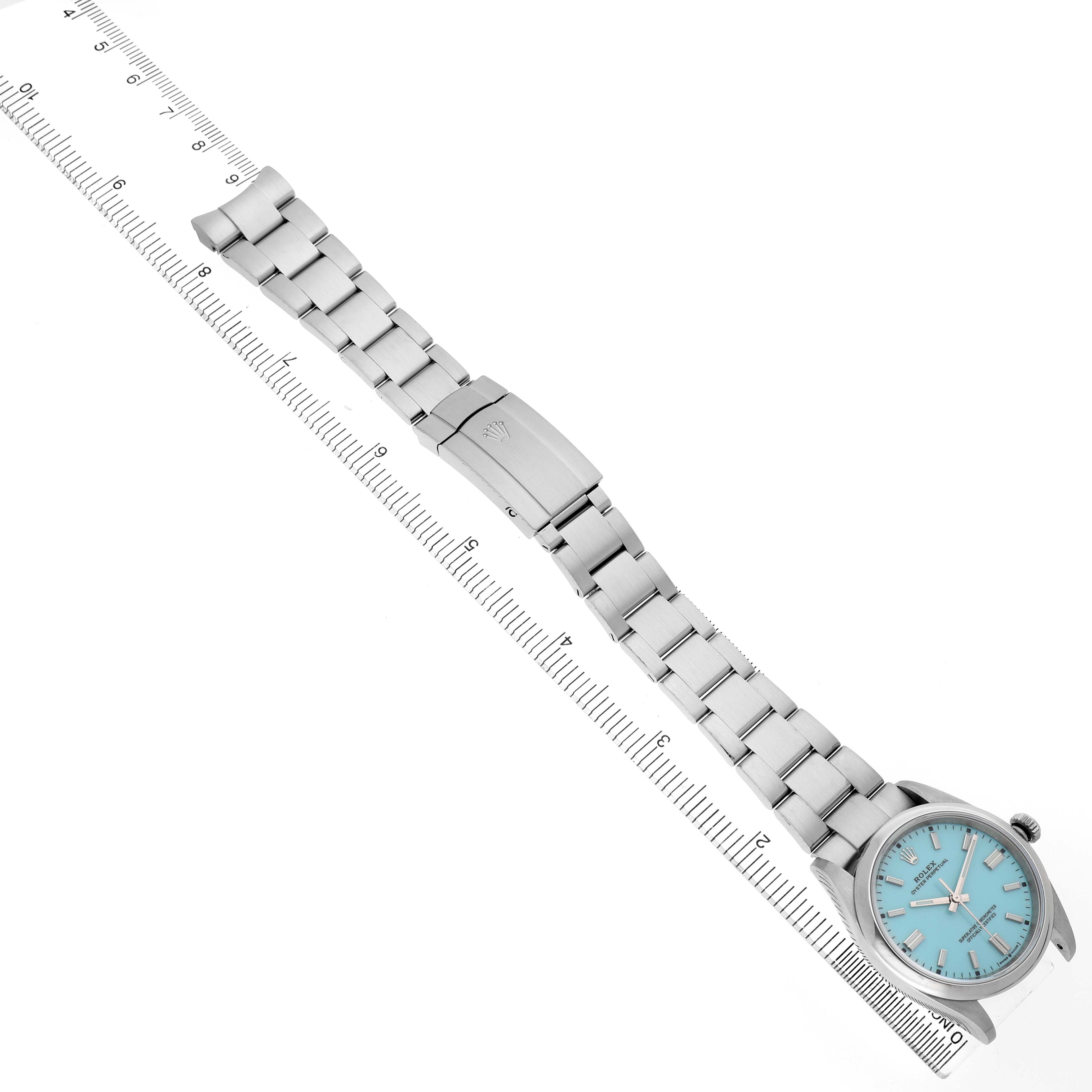 The Rolex Oyster Perpetual 126000 Men's Stainless Steel Blue Dial watch is shown from a top-down angle, featuring the full bracelet and clasp alongside a measuring scale.