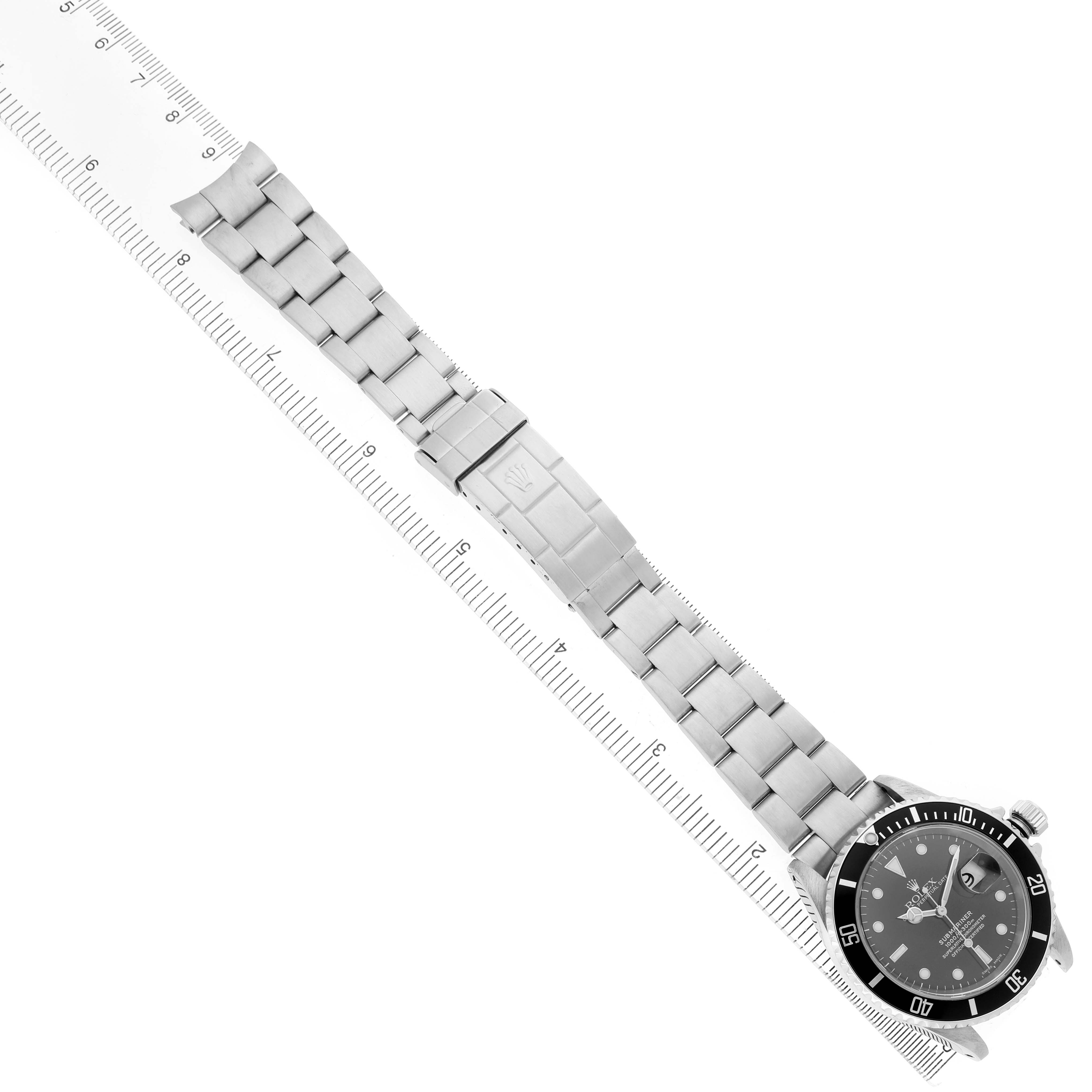 The Rolex Submariner 16610 Men's Stainless Steel Black Dial watch is shown from a top-down angle, displaying the face, bezel, and full bracelet alongside a ruler.