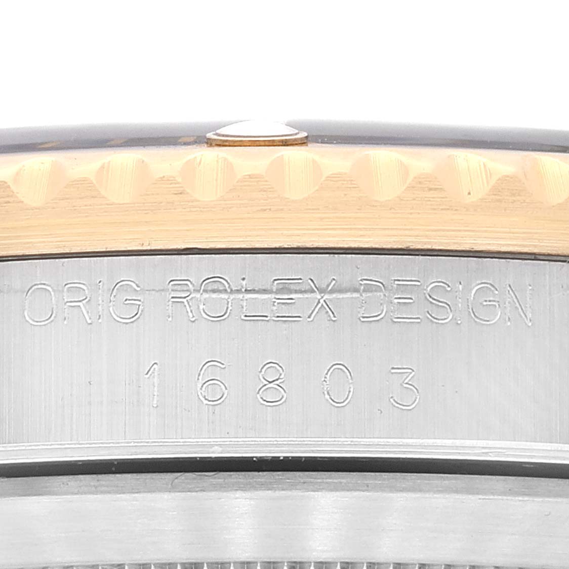 This image shows a close-up of the case side of a Rolex Submariner 16803 Men's Steel and Gold (two tone) Black Dial 16803 Men's Steel and Gold (two tone) Black Dial with the engraving "ORIG ROLEX DESIGN 16803".