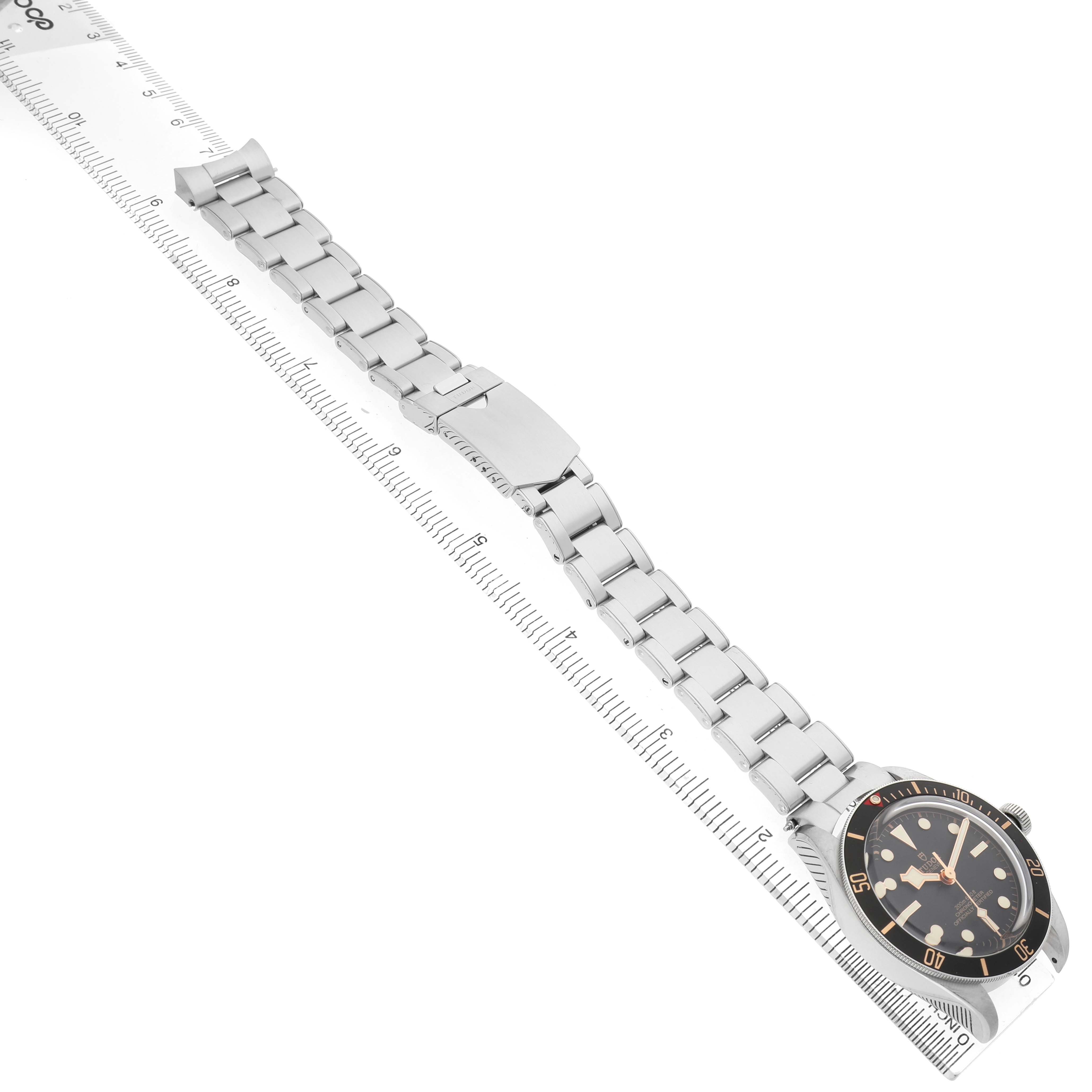 The image shows a Tudor Heritage Black Bay 79030 Men's Stainless Steel Black Dial watch laid flat with its full bracelet extended beside a ruler.