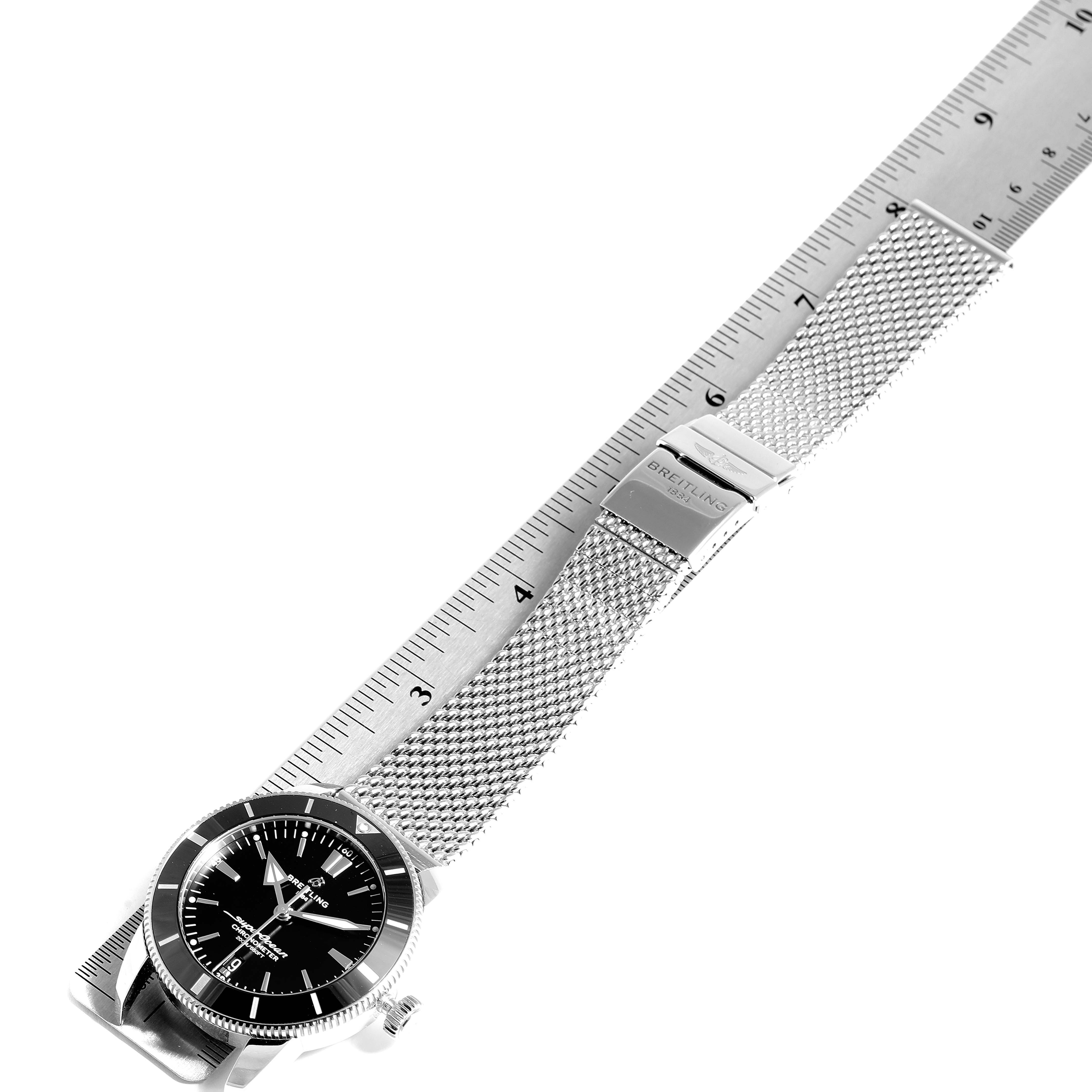 The Breitling Superocean AB2030 Men's Stainless Steel Black Dial AB2030 Men's Stainless Steel Black Dial watch is shown from an angled top view, displaying the face, bezel, and metal mesh strap beside a ruler.