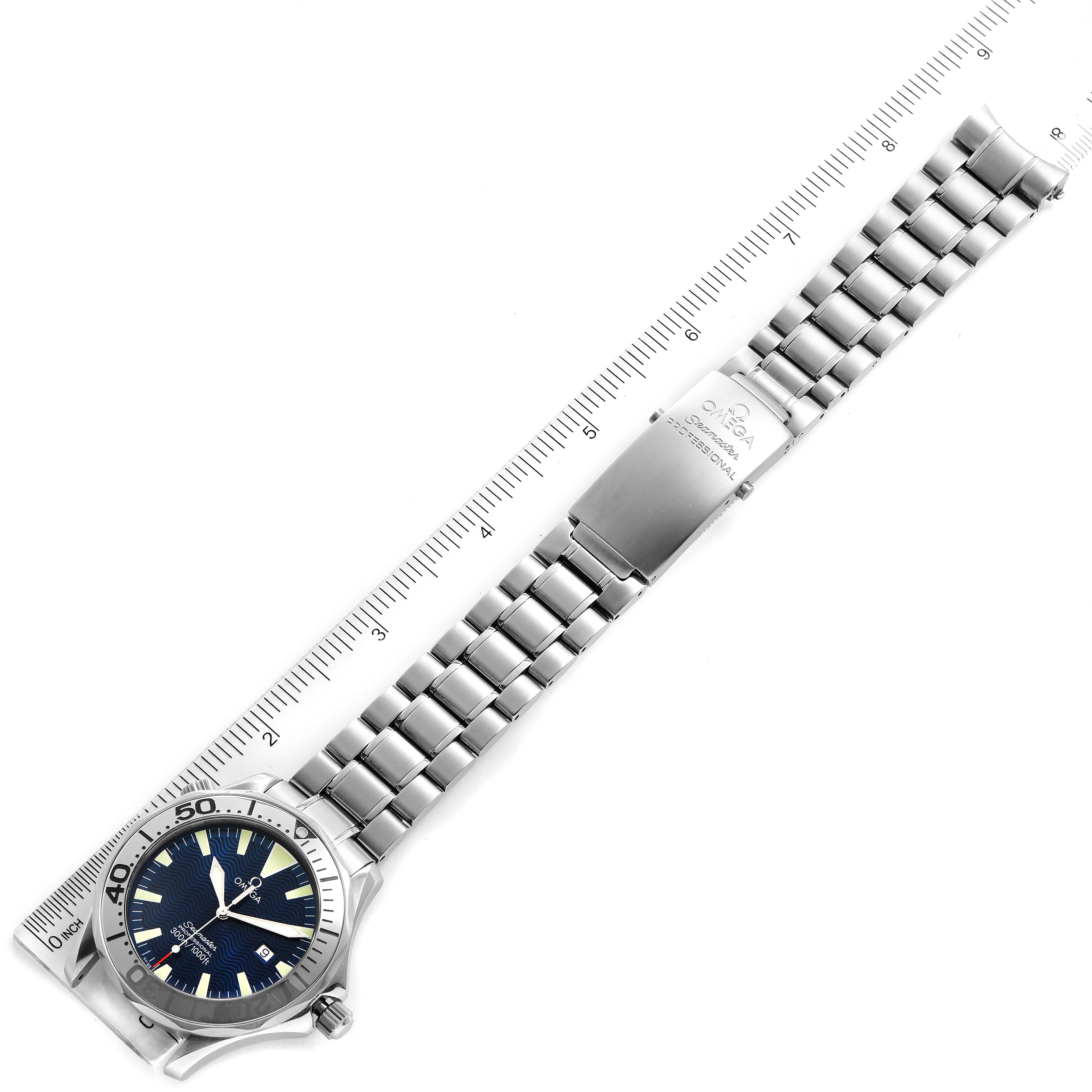 The Omega Seamaster 2265.80.00 Men
s Stainless Steel Blue Dial 2265.80.00 Men
s Stainless Steel Blue Dial watch is shown from a top-down angle, displaying its face, bezel, band, and clasp next to a ruler.