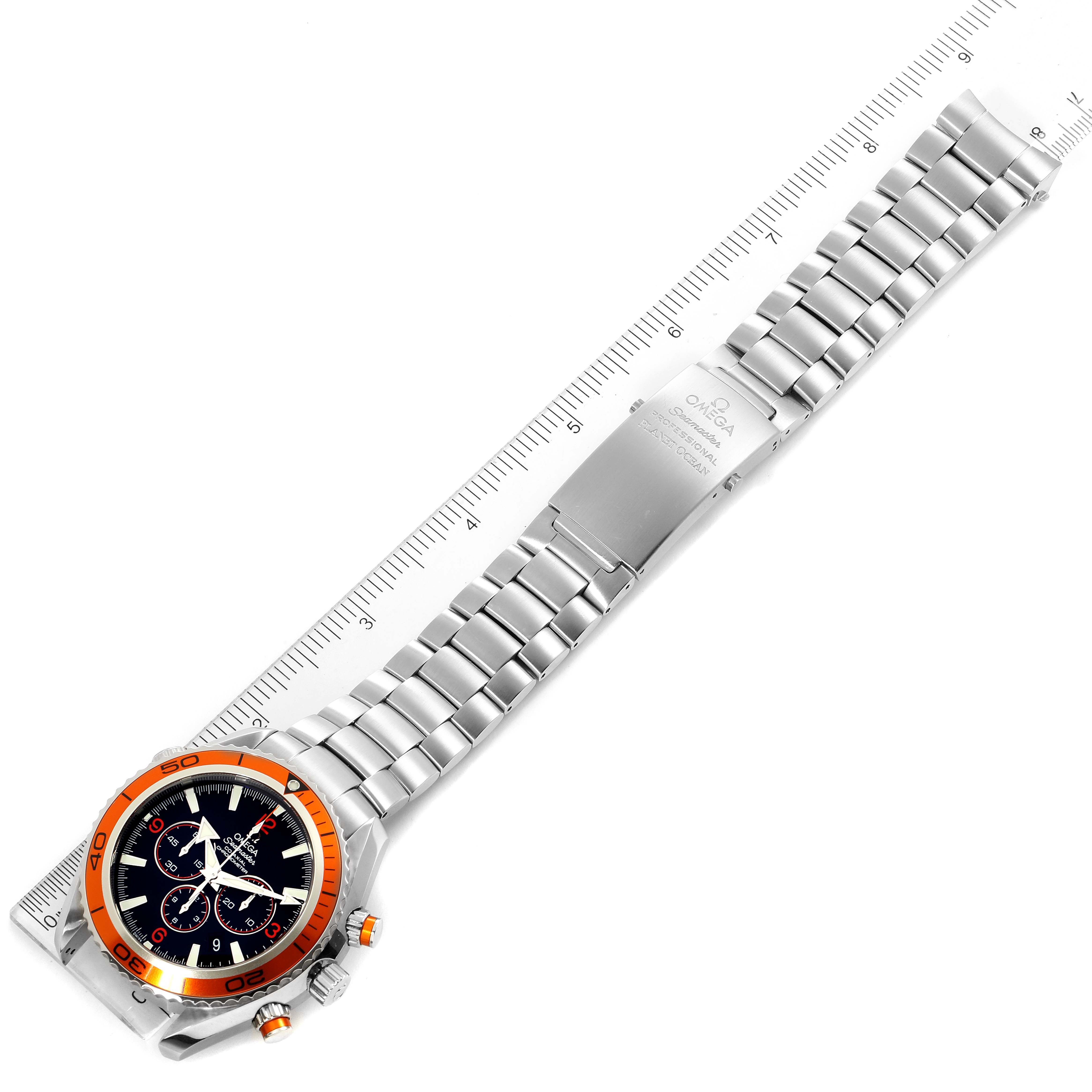 The image shows an overhead view of the Omega Planet Ocean 2218.50.00 Men
s Stainless Steel Black Dial 2218.50.00 Men
s Stainless Steel Black Dial watch, highlighting its full bracelet and watch face next to a ruler.